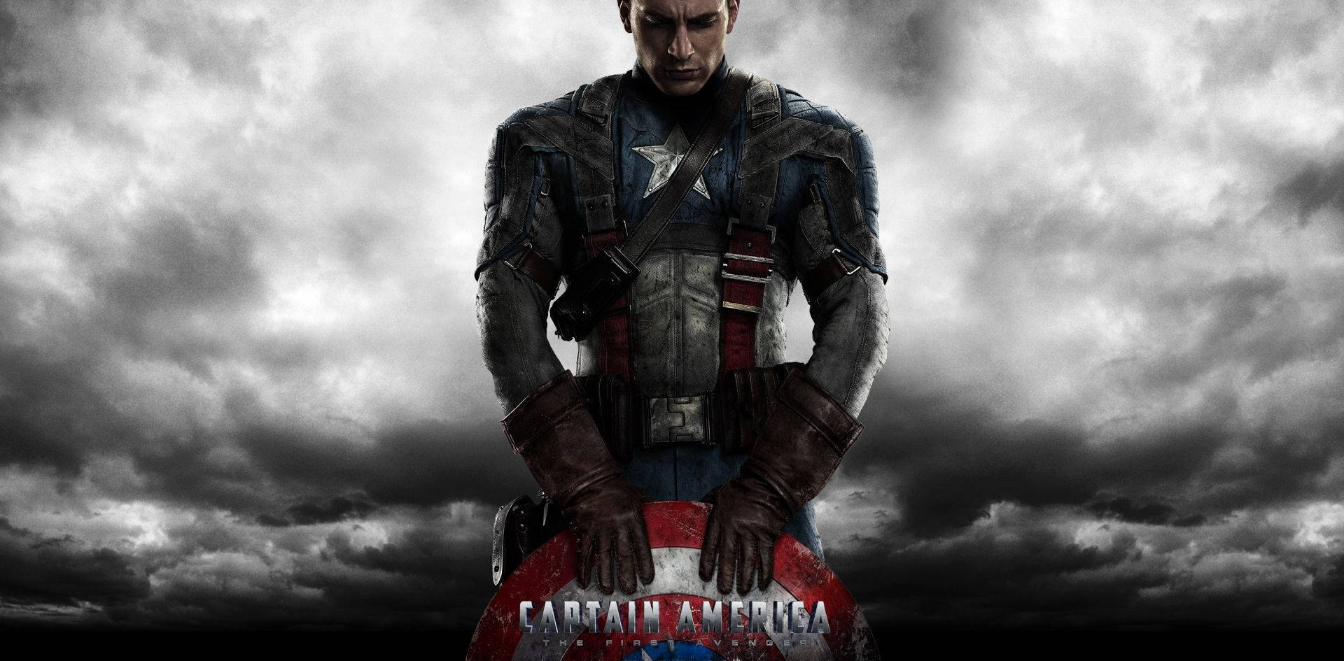 Marvel Captain America 桌布 壁紙 — 美國隊長在暴風般的灰色天空下莊嚴地站立，緊握盾牌，呈現出粗獷的電影風格肖像。