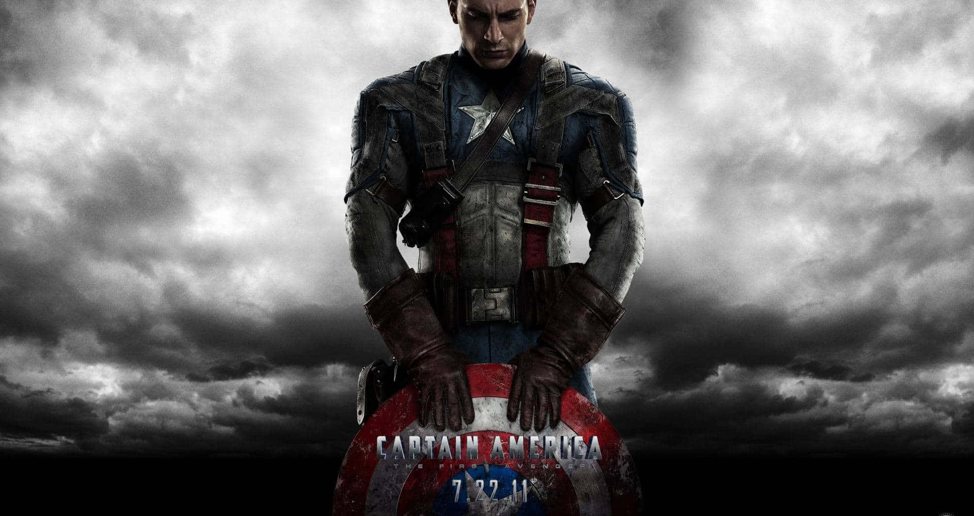 Captain America Cool 桌布 壁紙 — 美國隊長在暴風雨的灰色天空下莊嚴地站立，緊握盾牌，呈現出粗獷的電影風格肖像。
