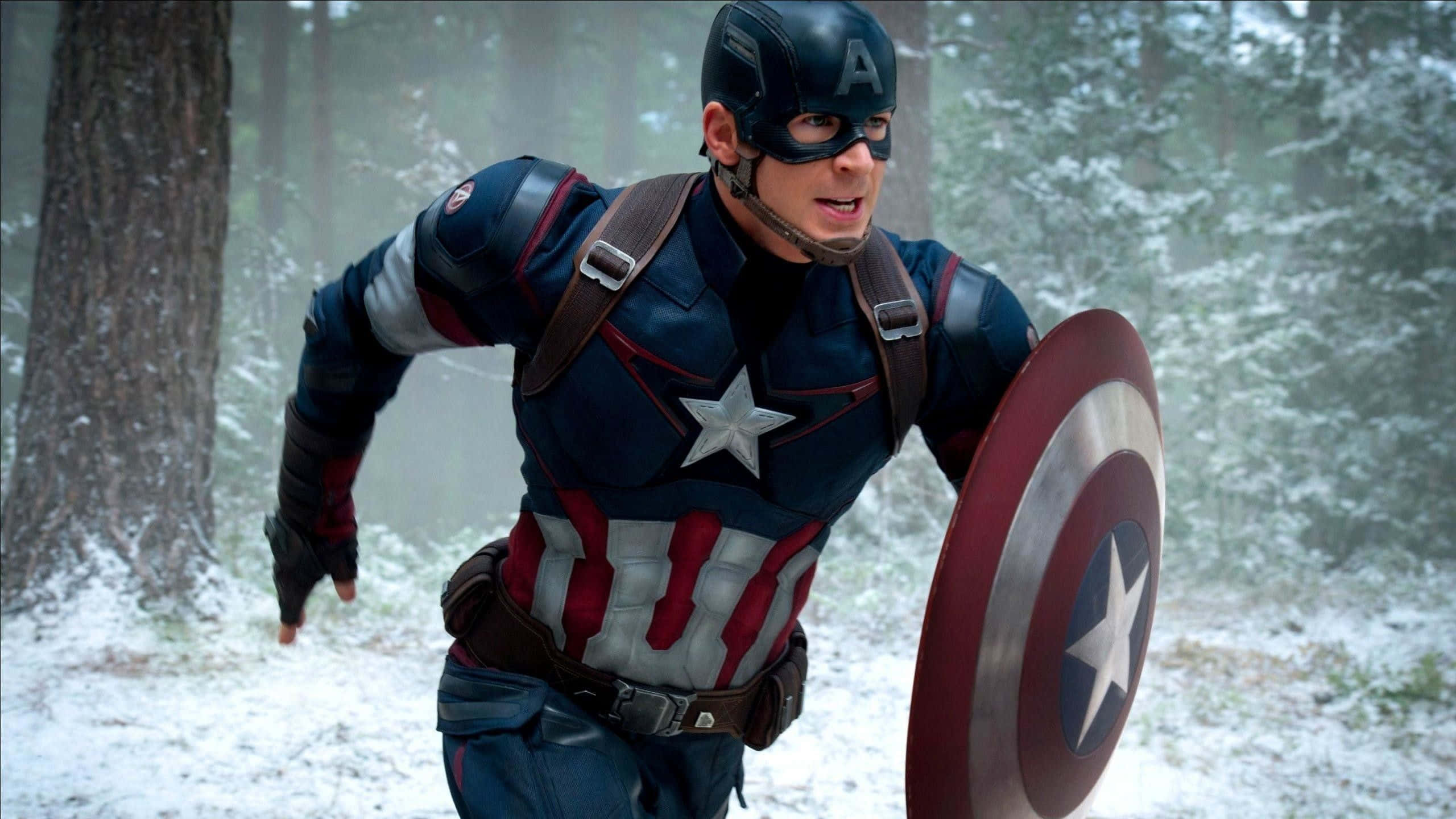 Captain America Desktop 桌布 壁紙 — 美國隊長在雪地森林中奔跑，手持標誌性盾牌，神情堅定。