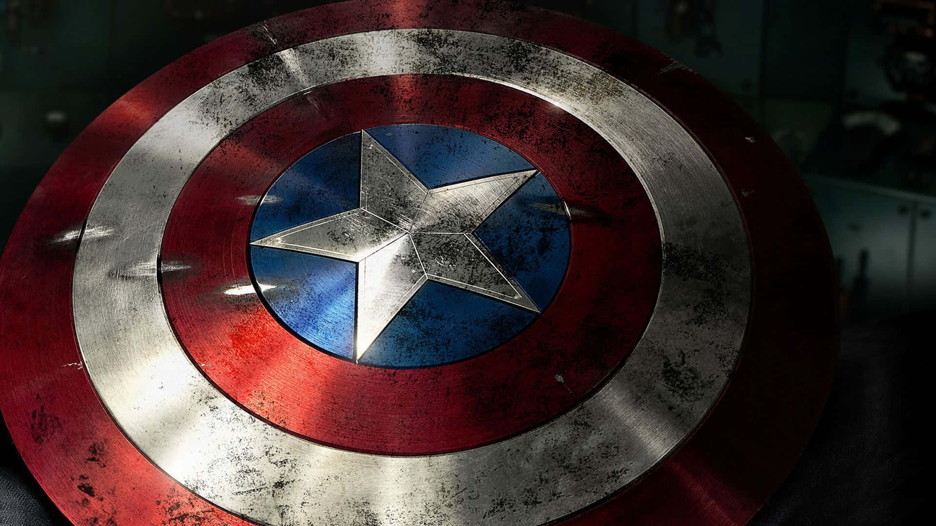 Captain America Logo 桌布 壁紙 — 美國隊長標誌性盾牌的特寫，在戲劇性燈光下顯示戰鬥造成的刮痕和凹痕。
