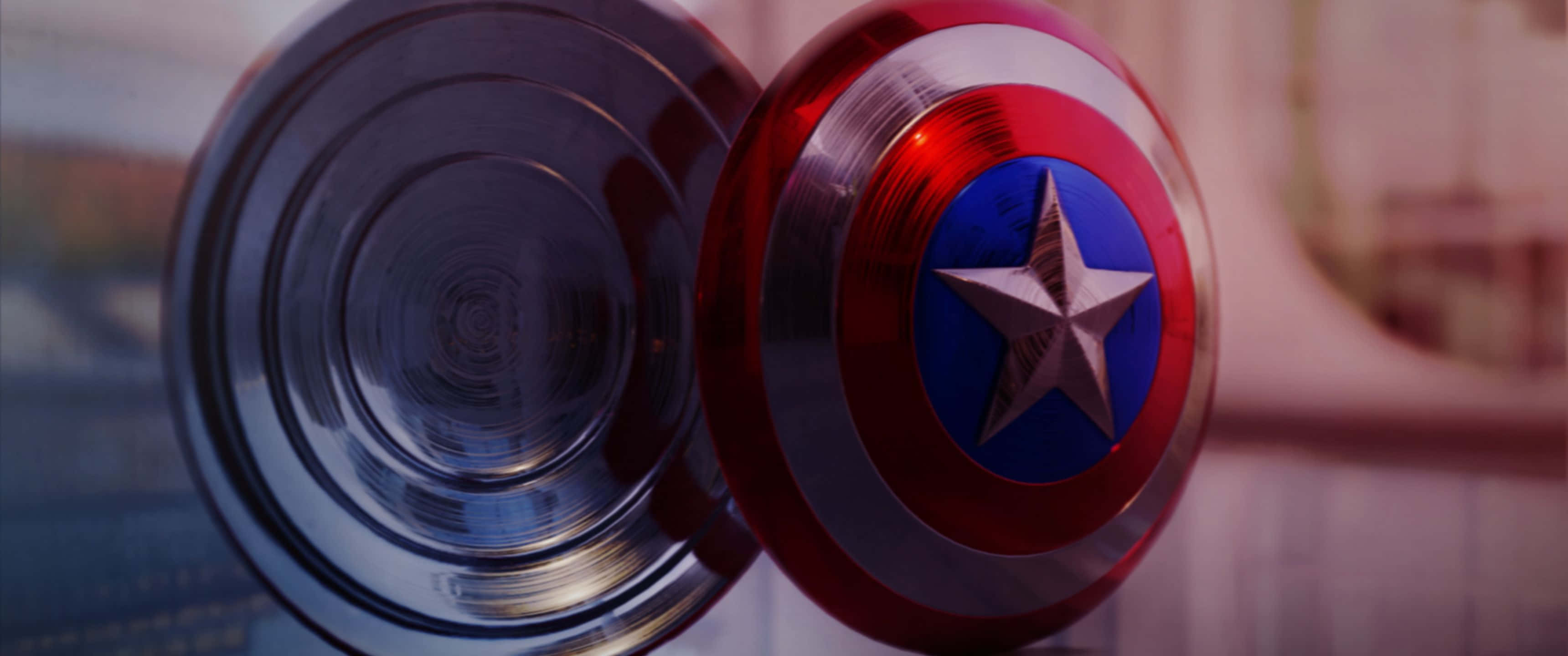 3440x1440p Captain America 桌布 壁紙 — 美國隊長標誌性紅白藍盾牌的特寫，中央有一顆銀星，置於金屬表面上。