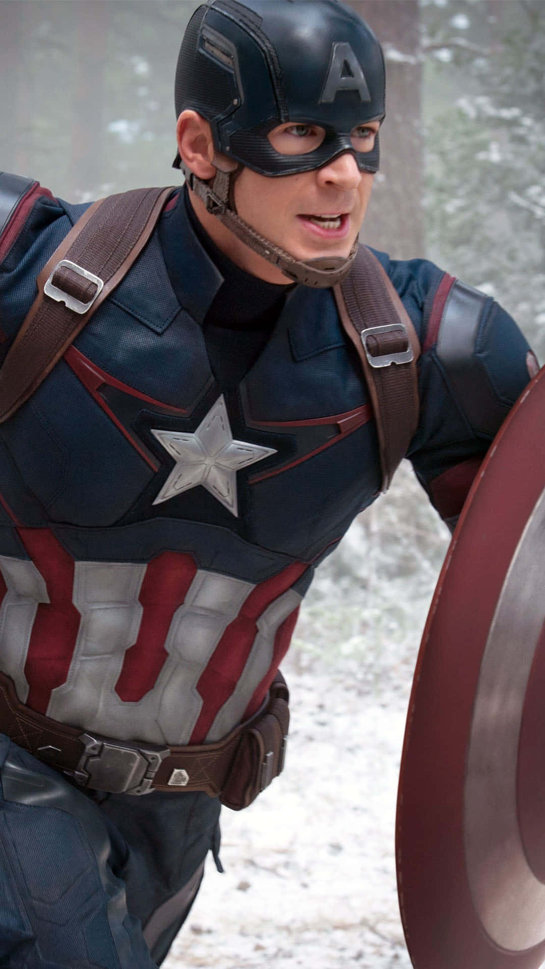 Captain America Android 桌布 壁紙 — 美國隊長穿著標誌性的紅白藍戰衣，在雪地森林中手持盾牌。