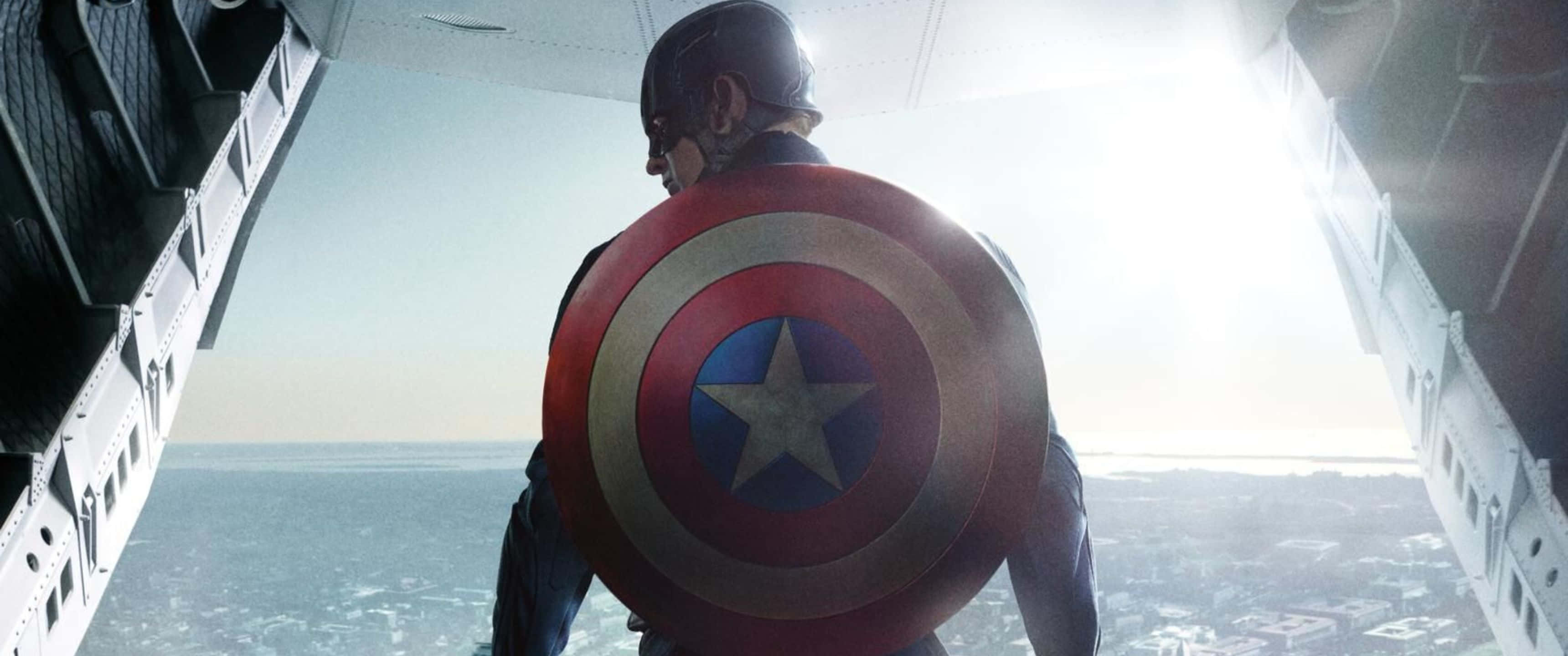 Marvel Movie 桌布 壁紙 — 美國隊長站在飛機艙門處，手持標誌性盾牌，俯瞰下方廣闊的城市。