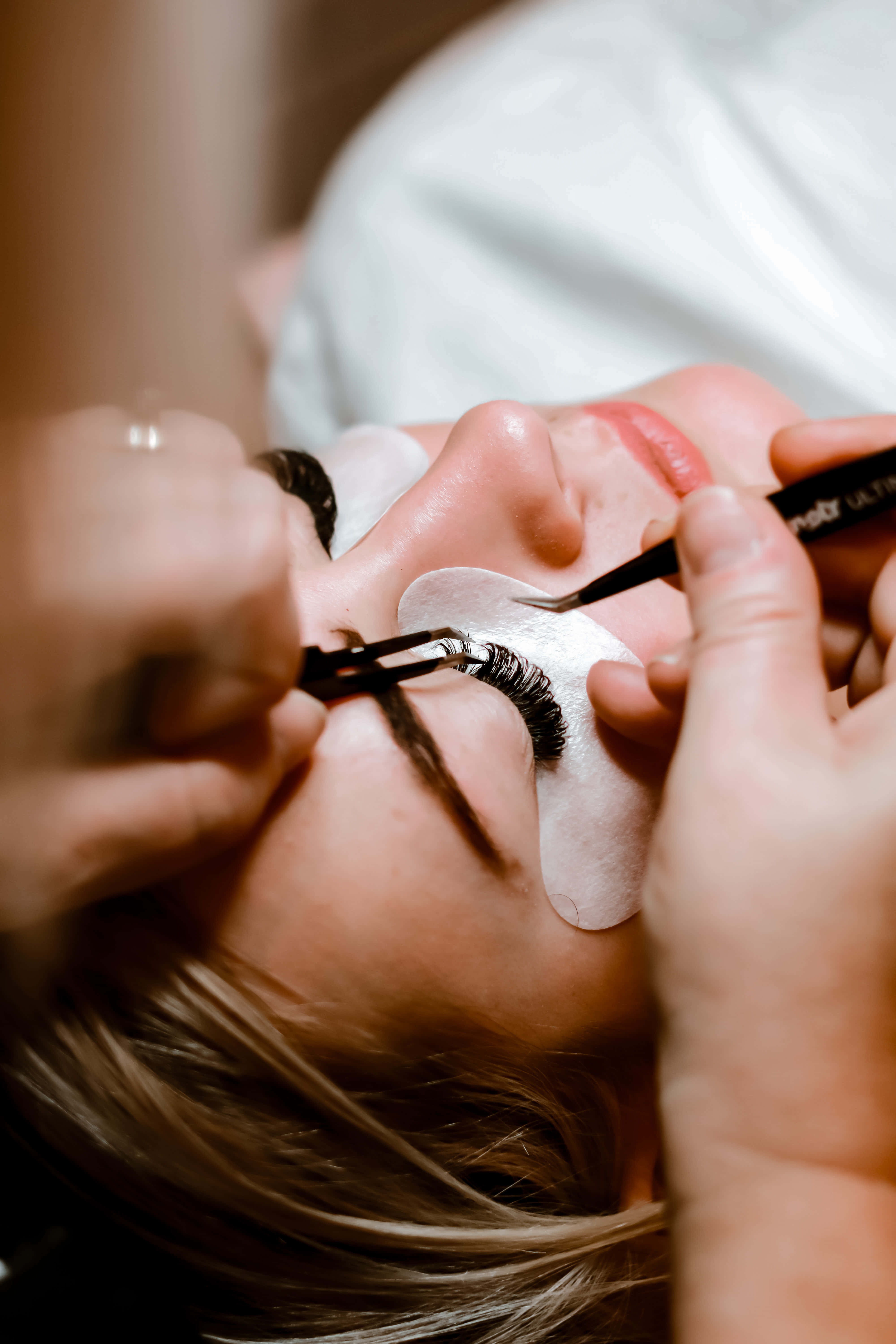 Beauty Salon 桌布 壁紙 — 美容院中，一個人正在用鑷子和睫毛刷貼假睫毛的特寫。