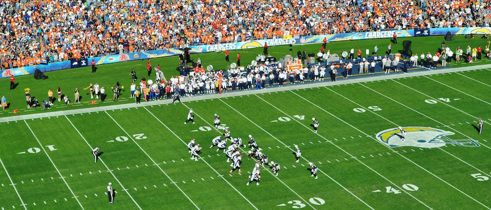 Cool NFL 桌布 壁紙 — 美式足球比賽期間，擠滿觀眾的體育館鳥瞰圖，球員在充滿活力的綠色場地上比賽。