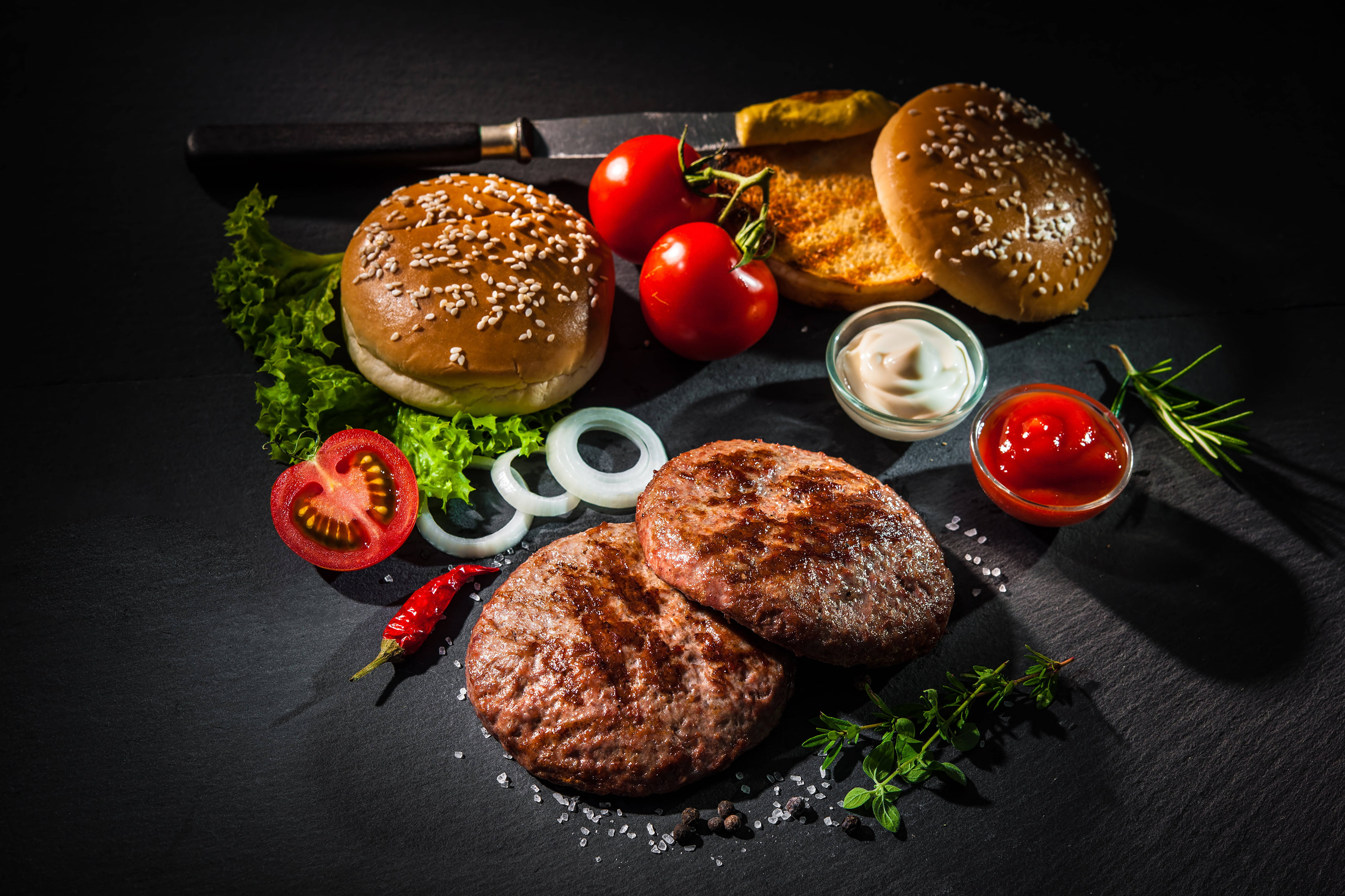 Food Photography 桌布 壁紙 — 美食漢堡配料在戲劇性燈光下，藝術地排列在深色石板之上，配以新鮮番茄、洋蔥、香草和醬汁。