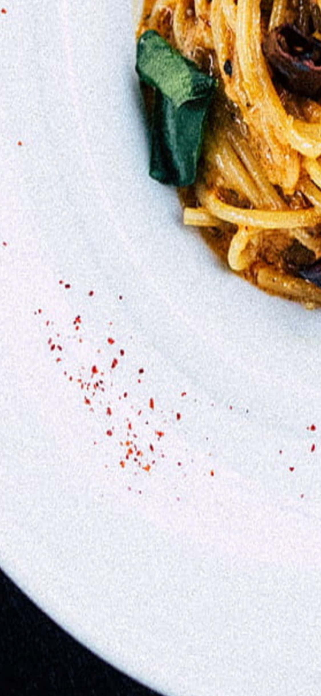 iPhone X Pasta 桌布 壁紙 — 義大利麵特寫，搭配羅勒葉和紅辣椒片，放在白色盤子上。