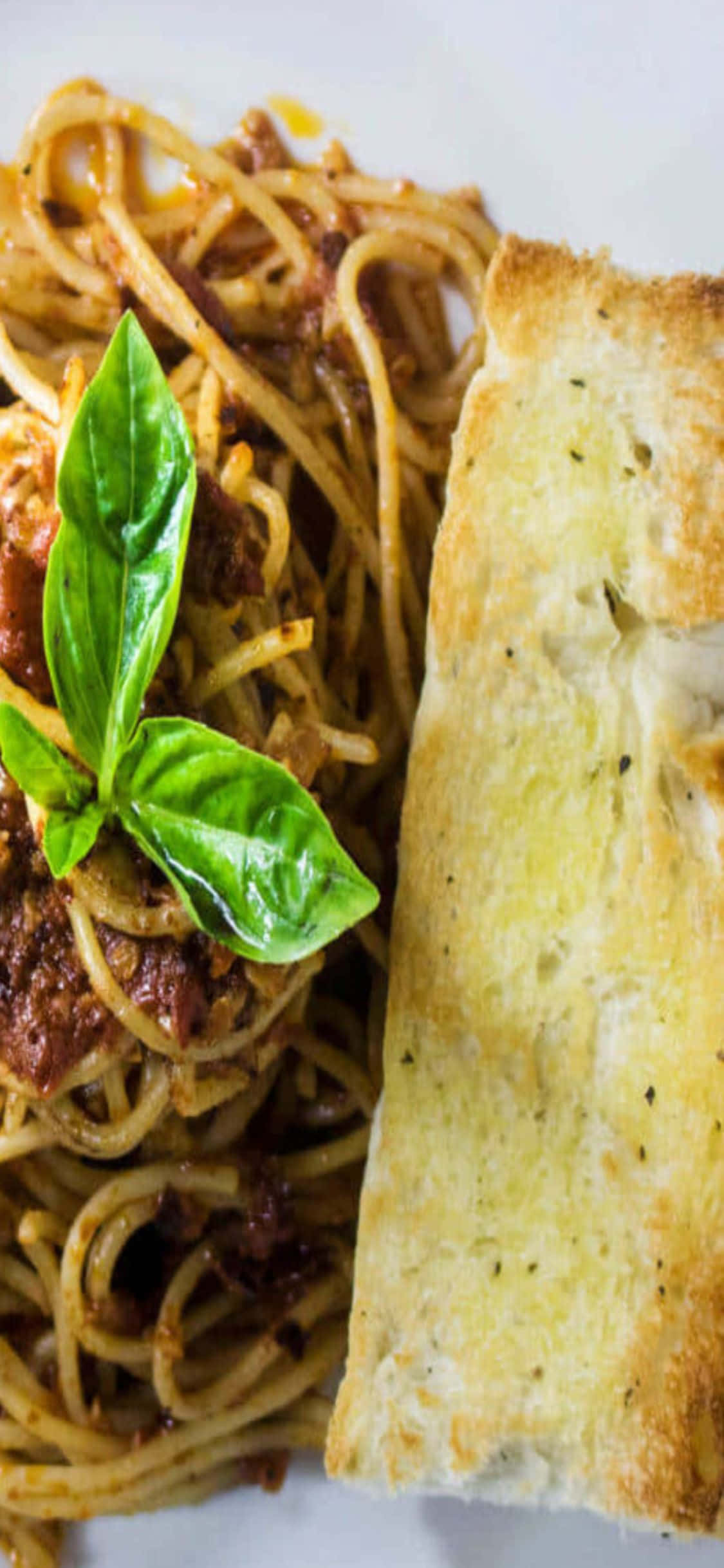 Spaghetti 桌布 壁紙 — 義大利麵配濃郁番茄醬和新鮮羅勒葉的特寫，旁邊有一片大蒜麵包。
