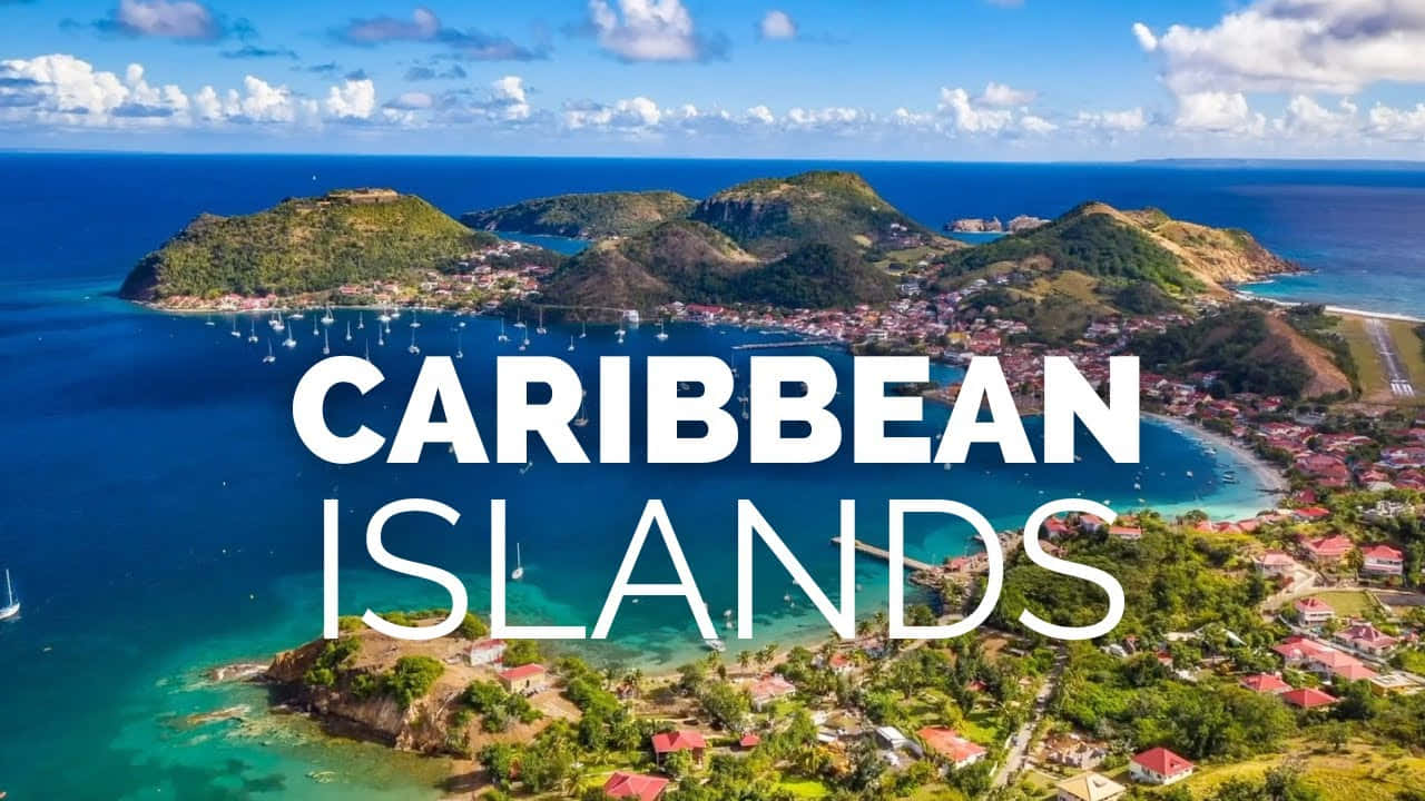 Caribbean Island 桌布 壁紙 — 翠綠加勒比海島嶼的鳥瞰圖，碧綠海水、帆船和色彩繽紛的房屋點綴在綠色山丘之間，天空湛藍明亮。