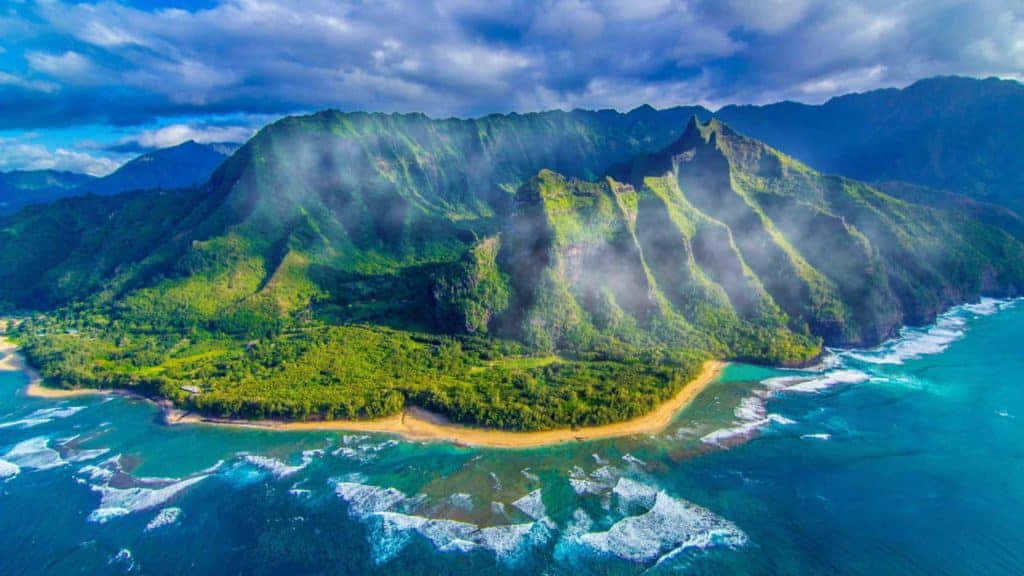 Hawaiian Island 桌布 壁紙 — 翠綠山巒與碧綠海洋交匯的航拍視角，霧氣在戲劇性雲層下的山峰周圍繚繞。