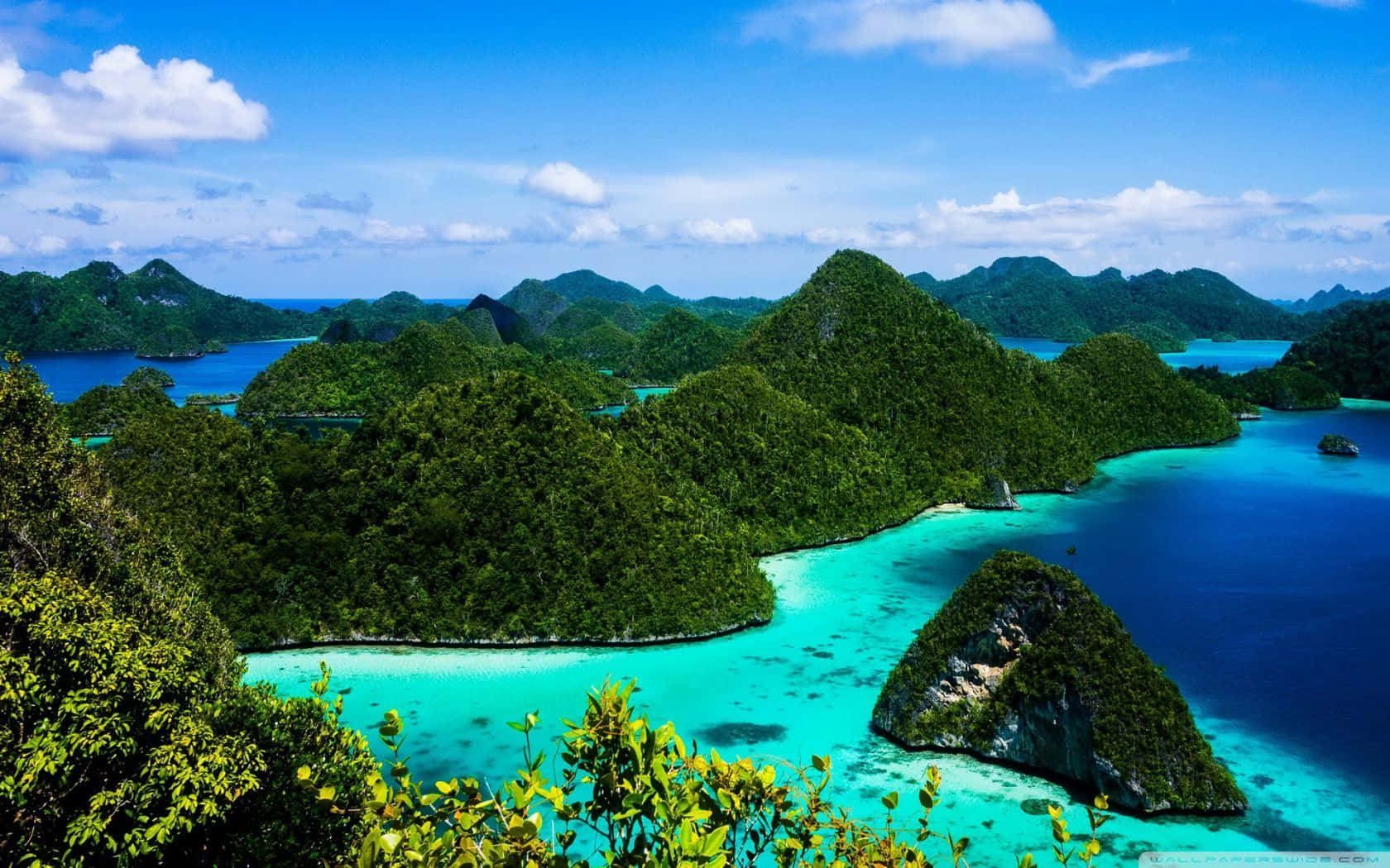 印尼 桌布 壁紙 — 翠綠的喀斯特島嶼從充滿活力的碧綠海水中升起，在明亮的藍天下有蓬鬆的白雲。