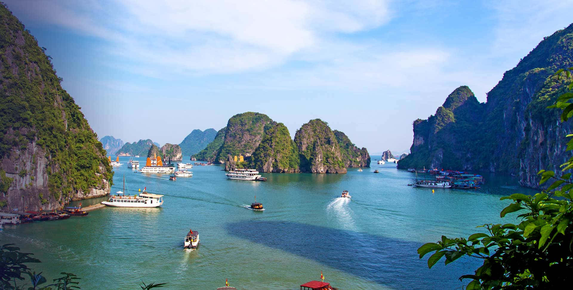 越南 桌布 壁紙 — 翠綠的喀斯特島嶼從碧綠的海水中升起，點綴著觀光船，天空湛藍明亮。