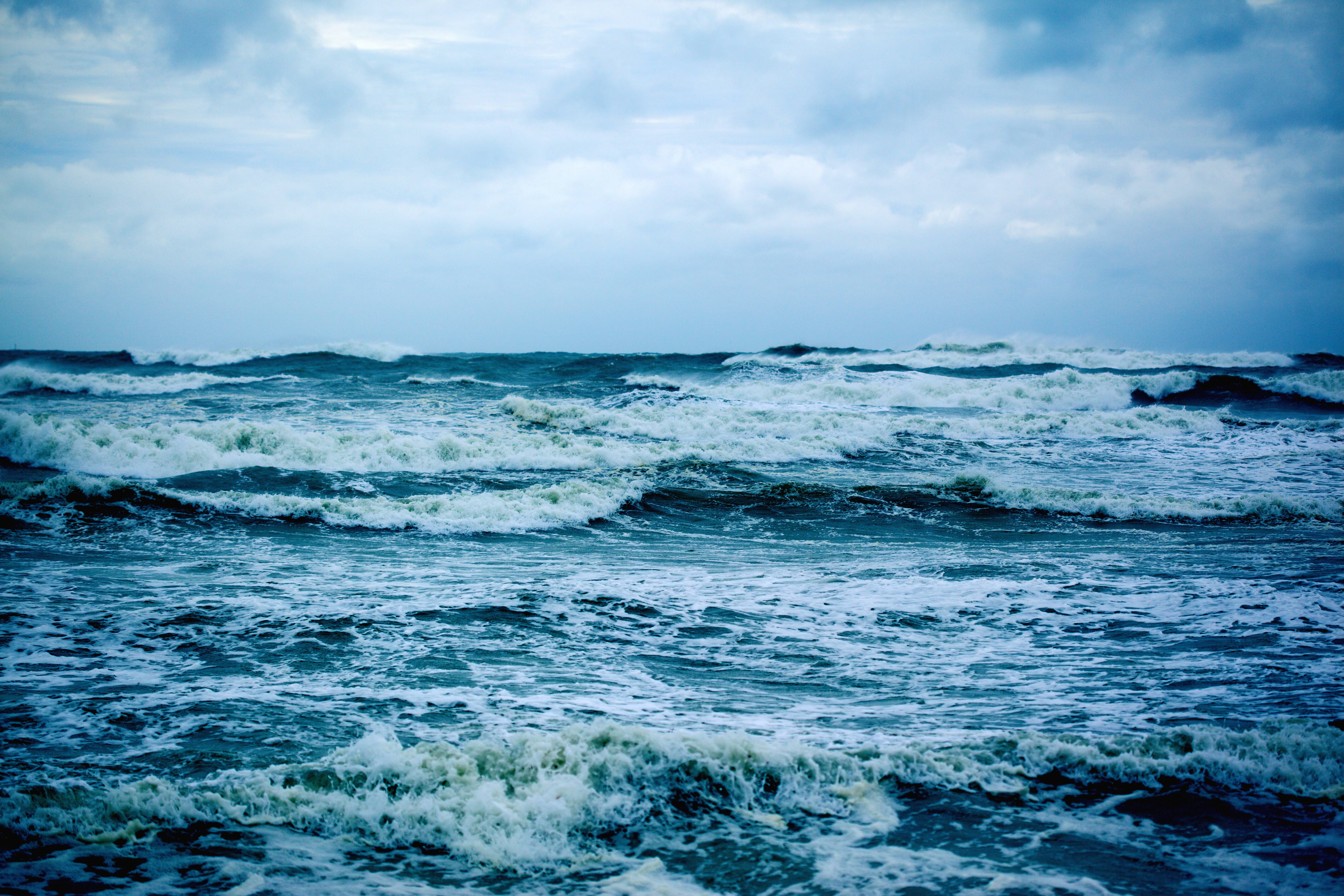 暴風 桌布 壁紙 — 翻騰的海浪在陰雲密佈的天空下撞擊，形成戲劇性的藍色調海景。