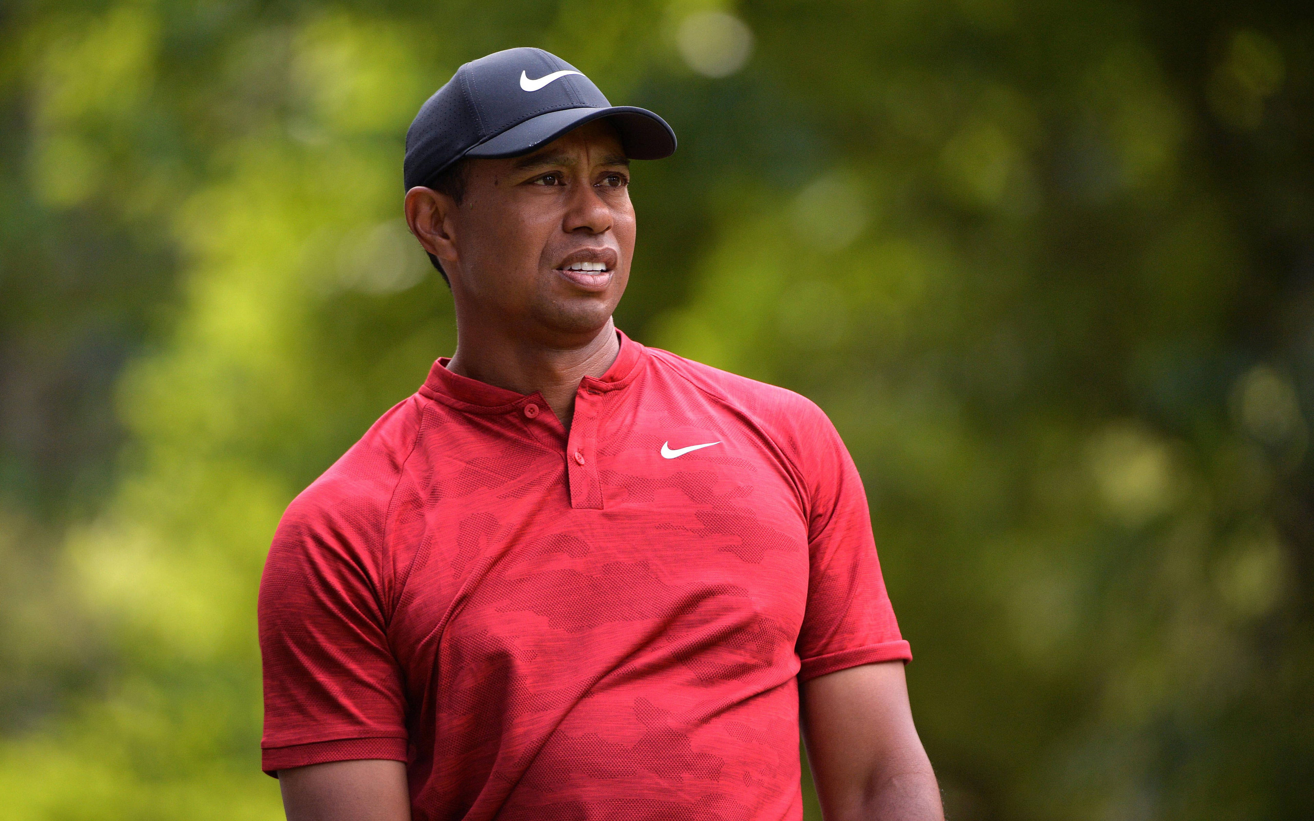 woods 桌布 壁紙 — 老虎伍茲穿著紅色Nike Polo衫和帽子，專注地站在模糊的綠色樹葉背景前。
