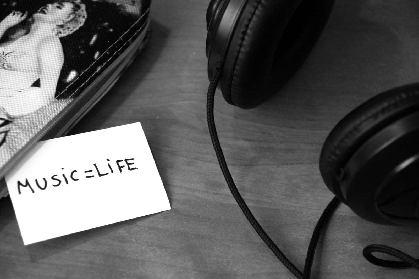 Black And White Music 桌布 壁紙 — 耳機、手寫便條寫著音樂等於生命，以及一個有圖案的小袋放在有紋理的表面上的黑白靜物。