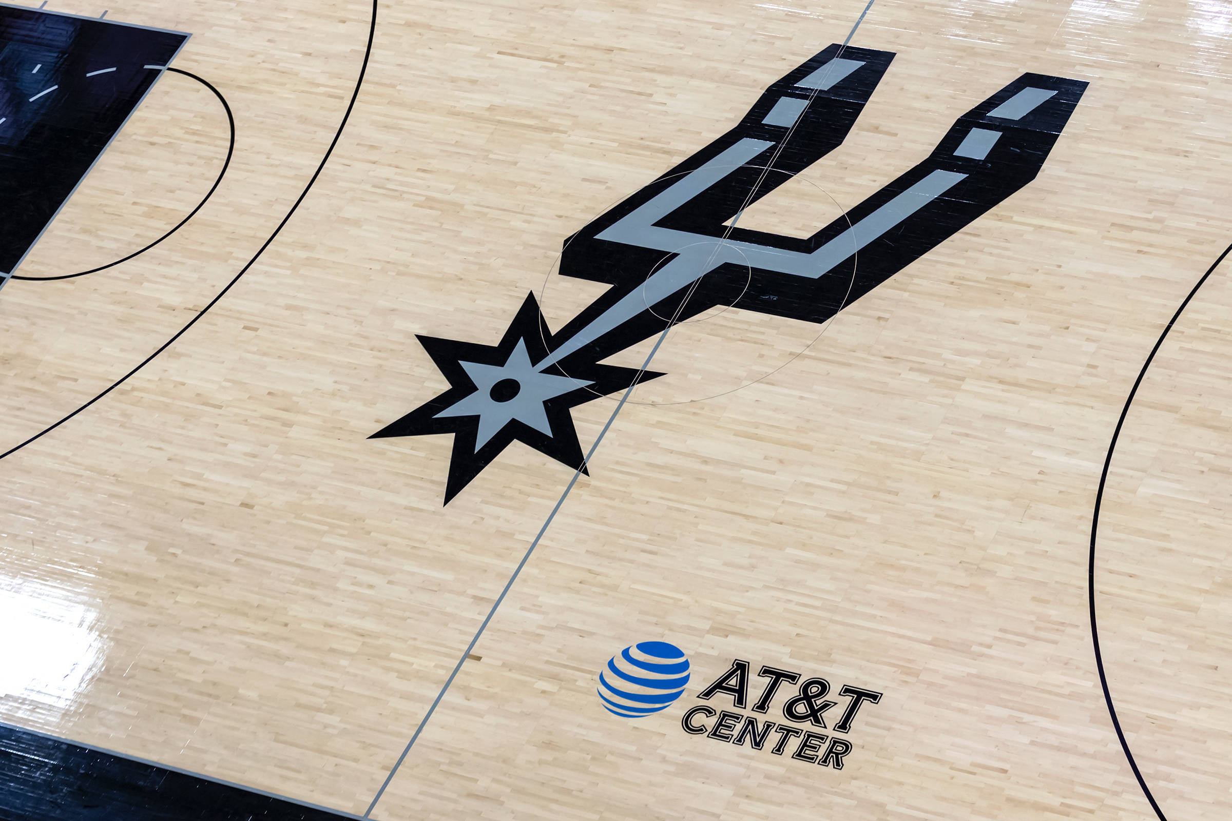 Spurs 桌布 壁紙 — 聖安東尼奧馬刺隊標誌在拋光木製籃球場上的特寫，帶有AT&T中心品牌標識。