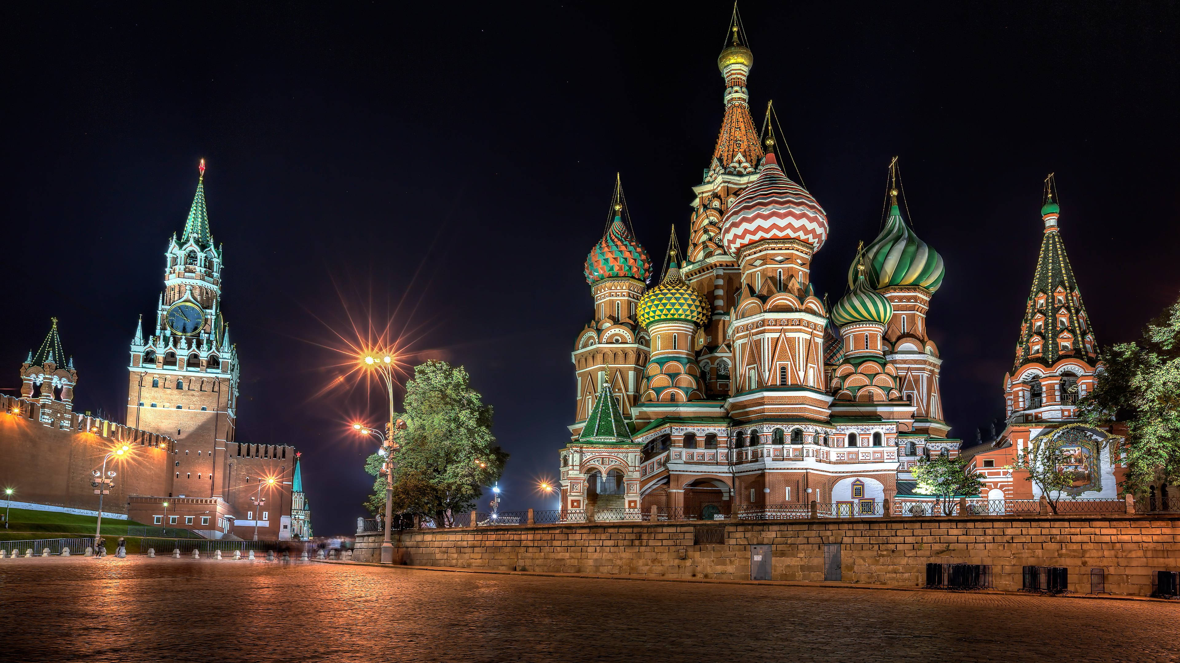 Russia 桌布 壁紙 — 聖巴西爾大教堂在夜間亮起，其色彩繽紛的洋蔥形圓頂在黑暗的天空下閃耀，旁邊是克里姆林宮塔樓。