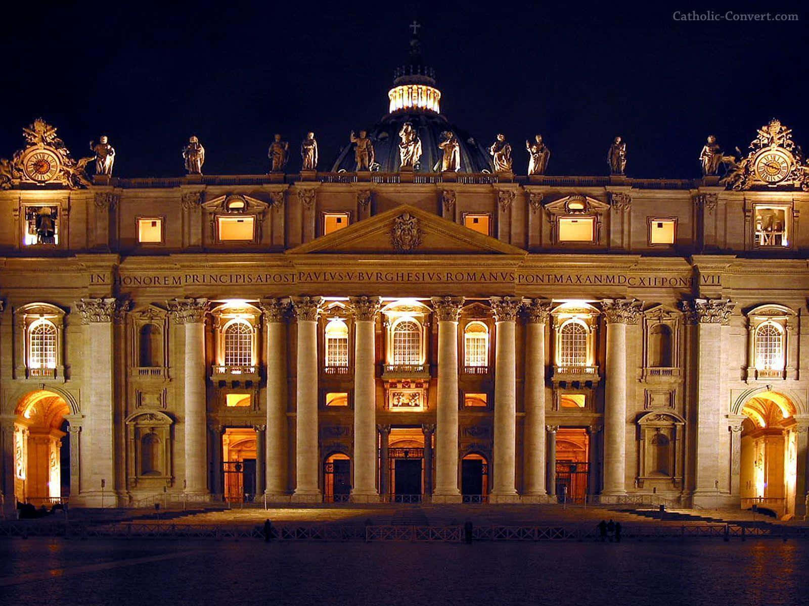 Catholic Desktop 桌布 壁紙 — 聖彼得大教堂夜間宏偉的燈光外牆，發光的柱子和雕像映襯著黑暗的天空。