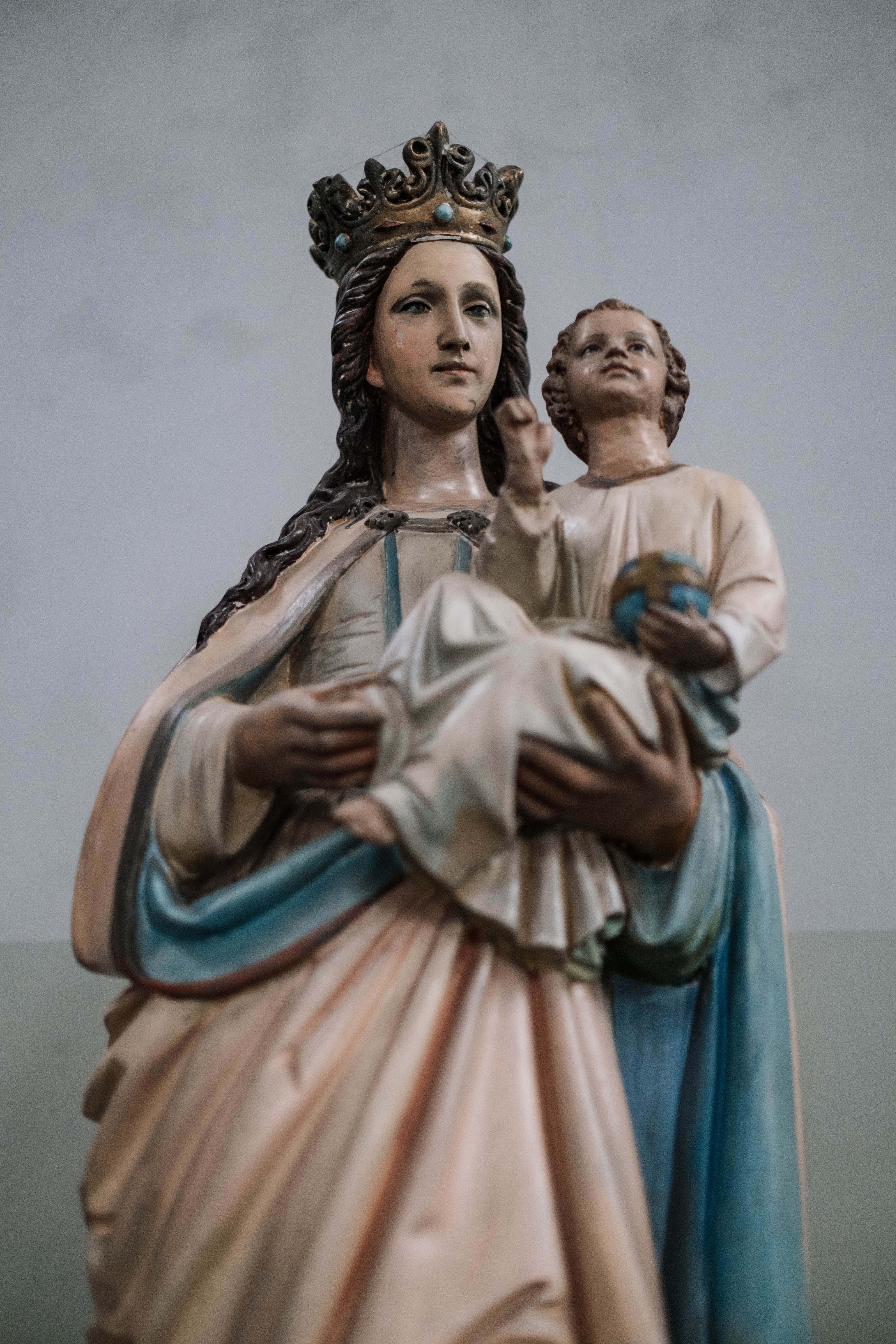 Mother Mary 桌布 壁紙 — 聖母瑪利亞懷抱嬰兒耶穌的寧靜雕像，兩者均戴冠冕，披著柔和的桃色和藍色長袍。