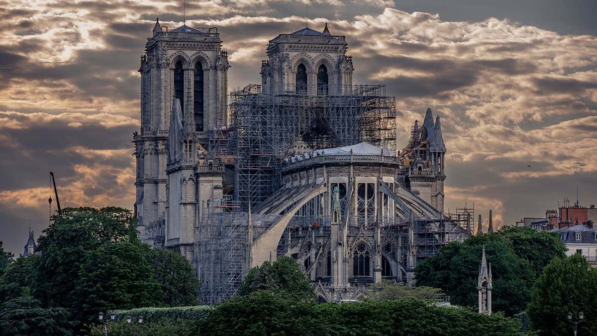 Gothic Architecture 桌布 壁紙 — 聖母院大教堂在戲劇性的暮色天空下矗立，廣泛的鷹架覆蓋其受損的屋頂和尖塔。