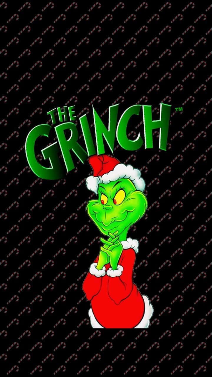 Cute Grinch 桌布 壁紙 — 聖誕怪傑戴著紅色聖誕帽和袋子，在黑色糖果棒圖案背景前頑皮地微笑。