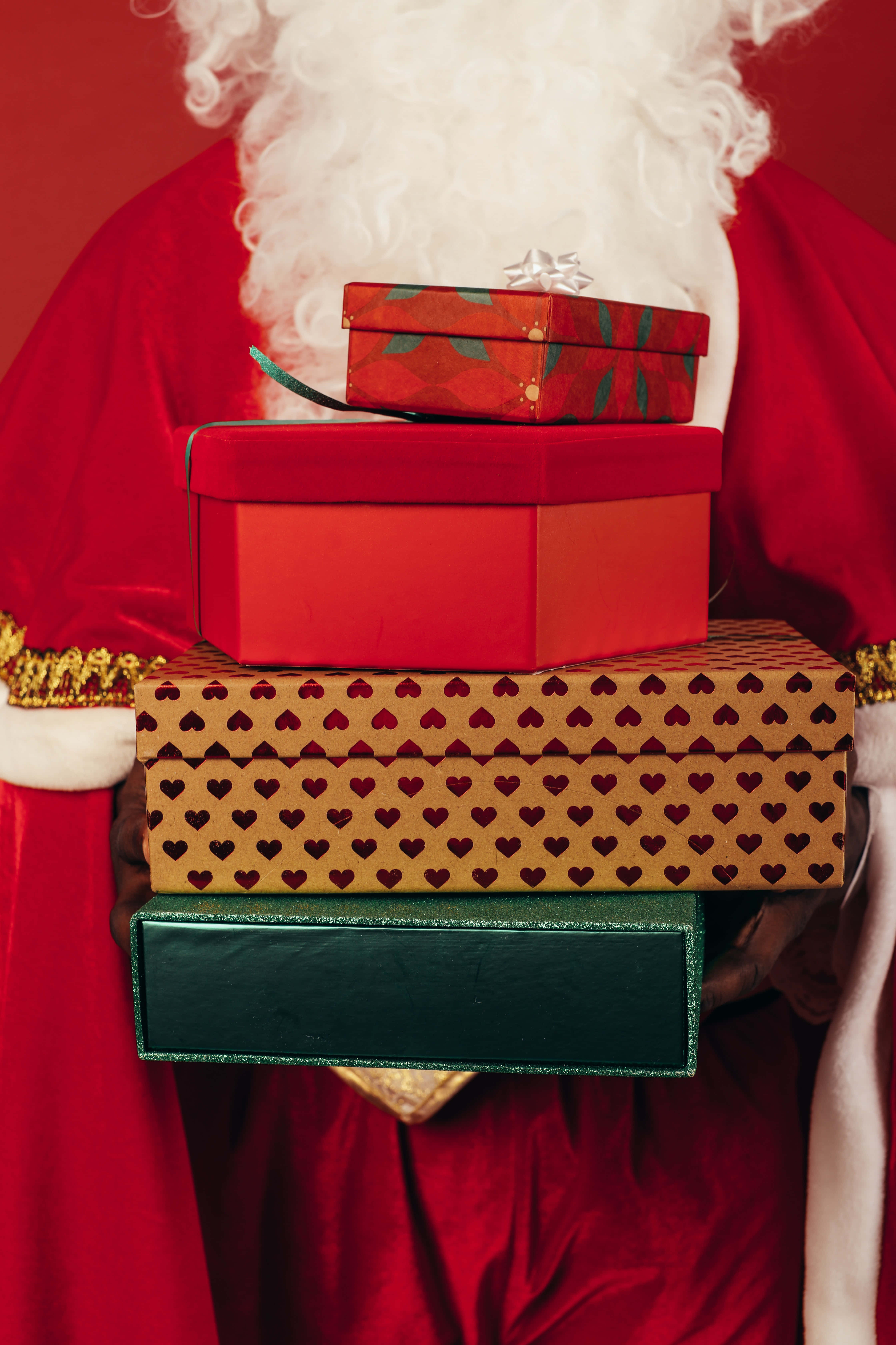 Santa Claus 桌布 壁紙 — 聖誕老人在鮮紅色背景前拿著一疊色彩繽紛的禮物盒。