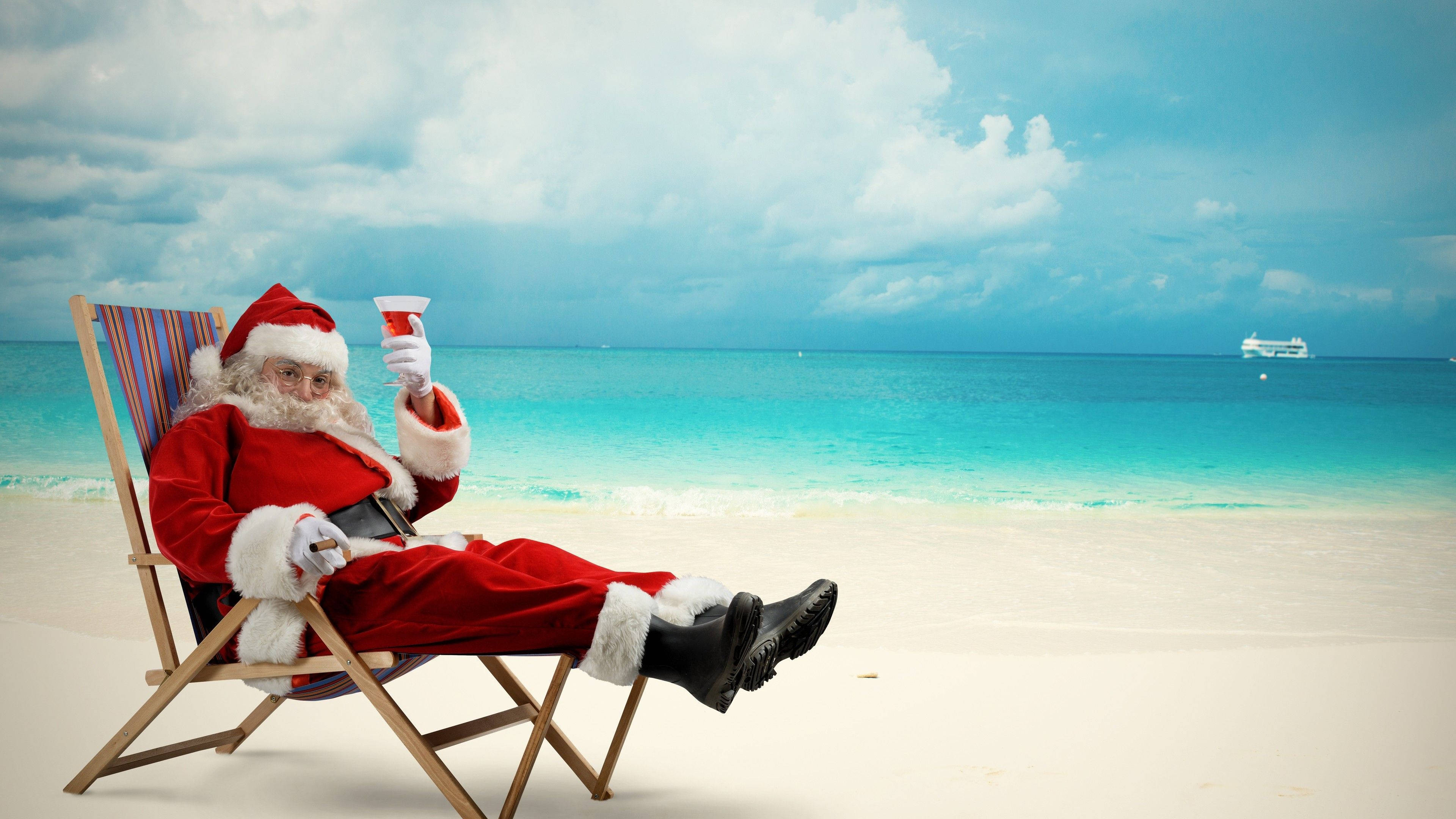 Santa Claus 桌布 壁紙 — 聖誕老人坐在沙灘椅上，在碧綠海洋和多雲天空的背景下啜飲飲料。