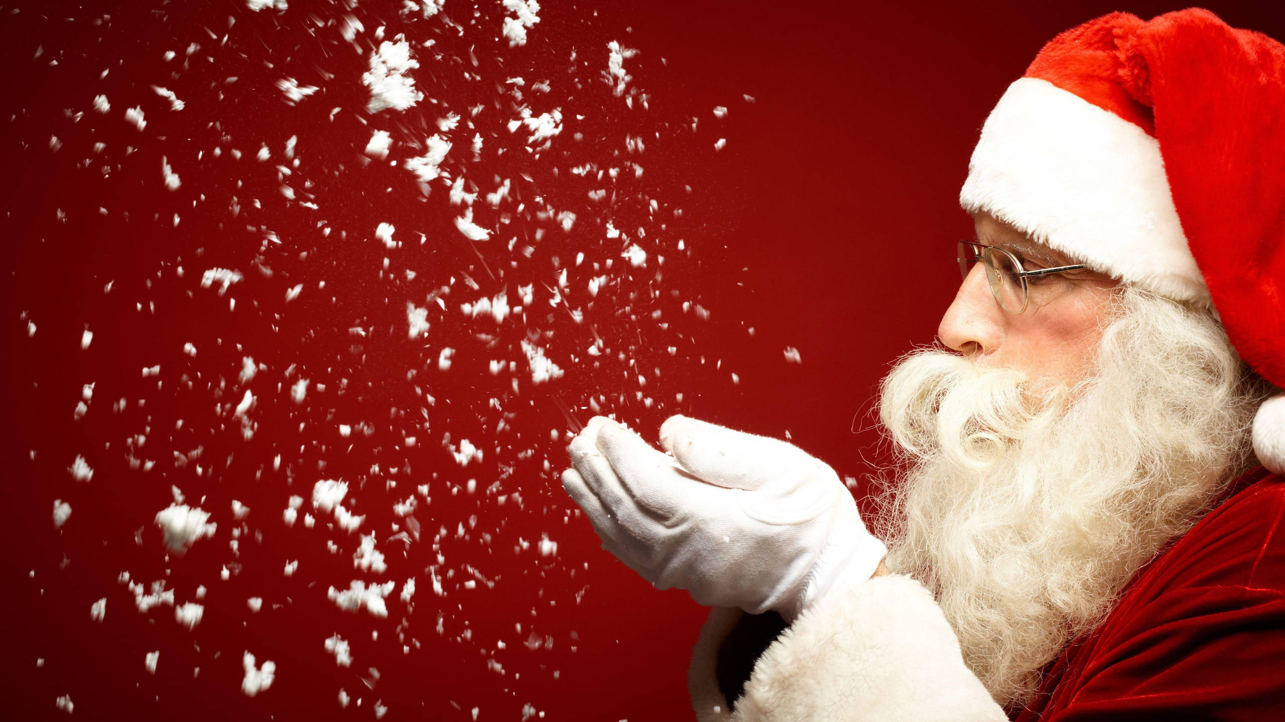 Santa Claus 桌布 壁紙 — 聖誕老人從戴手套的手吹出雪花，襯托鮮豔的紅色背景。