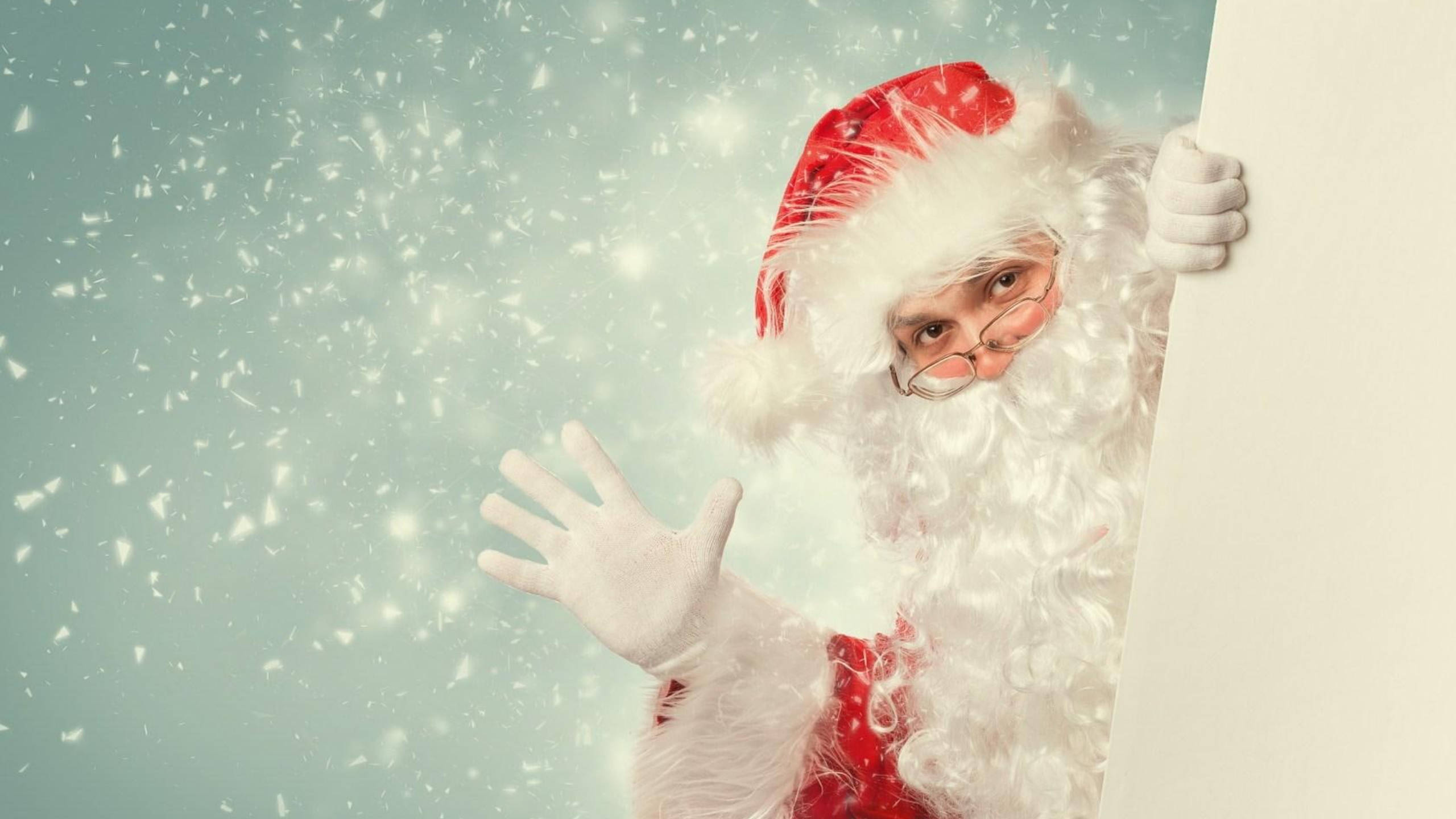 Santa Claus 桌布 壁紙 — 聖誕老人從白色板後探出頭來，雪花在柔和的青綠色背景中飄落。
