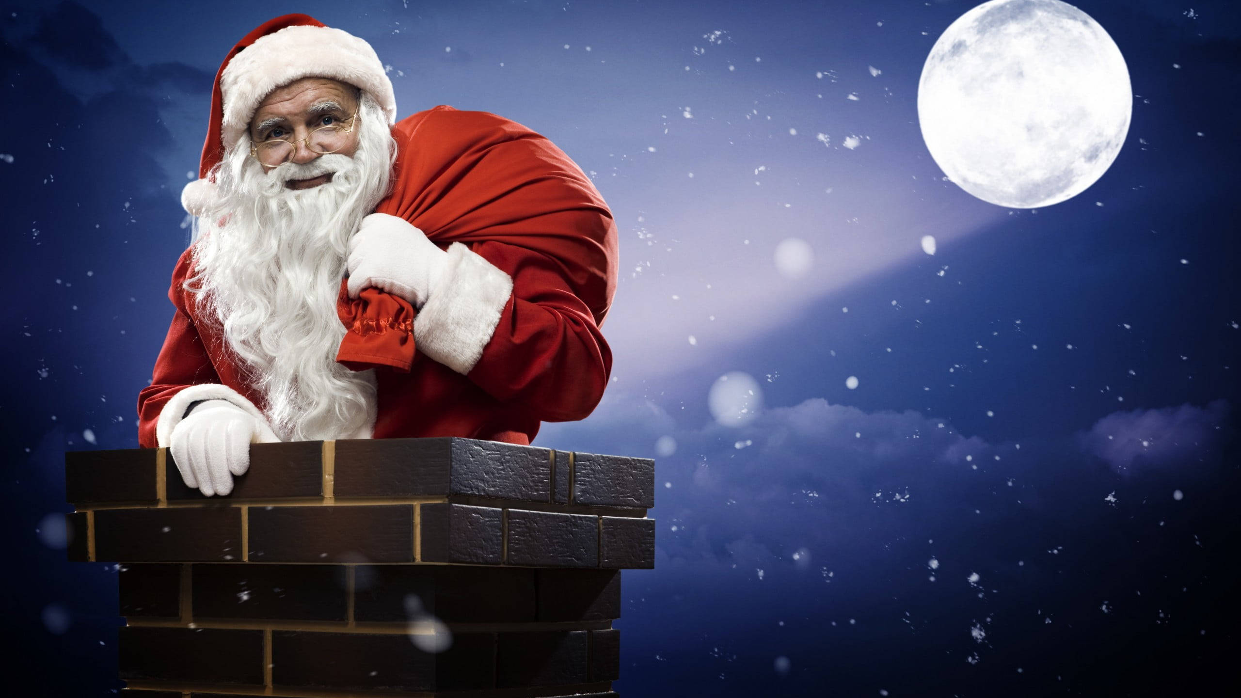 Santa 桌布 壁紙 — 聖誕老人從磚砌煙囪中探出頭來，背景是雪花飄落的雪夜月光夜空。