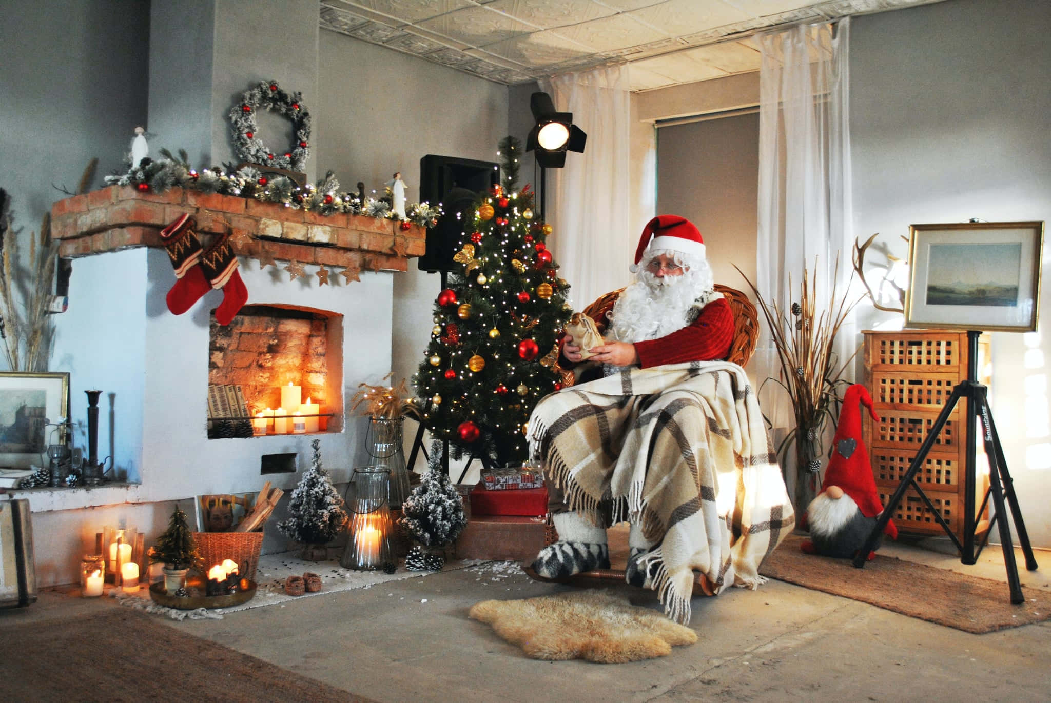 Teams Christmas 桌布 壁紙 — 聖誕老人溫暖地裹著格紋毯，坐在發光的壁爐和裝飾好的聖誕樹旁。
