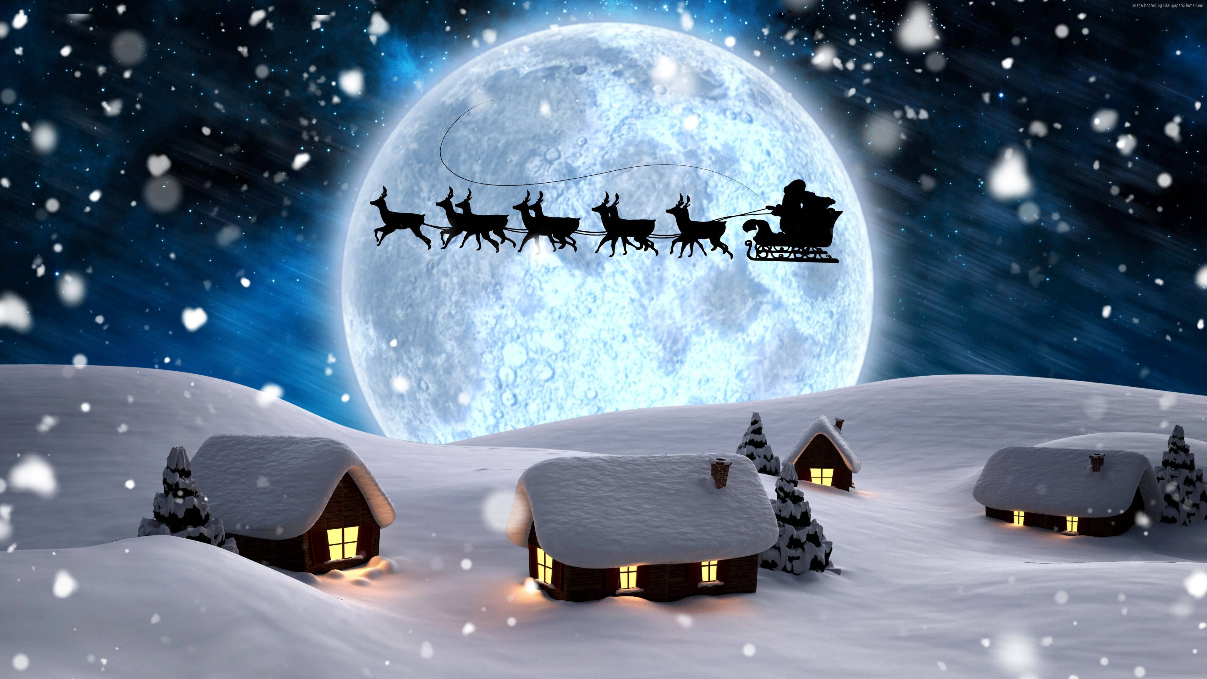 Santa Claus 桌布 壁紙 — 聖誕老人的雪橇飛過一輪巨大的月亮，下方是積雪覆蓋的小屋，窗戶透出溫暖的光芒，雪花飄落。