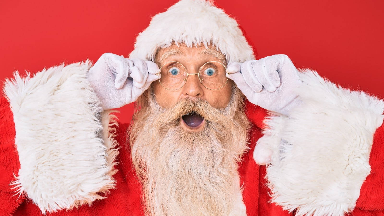 Santa Claus 桌布 壁紙 — 聖誕老人睜大眼睛，張開嘴巴，驚訝地拿著眼鏡，背景為純紅色。
