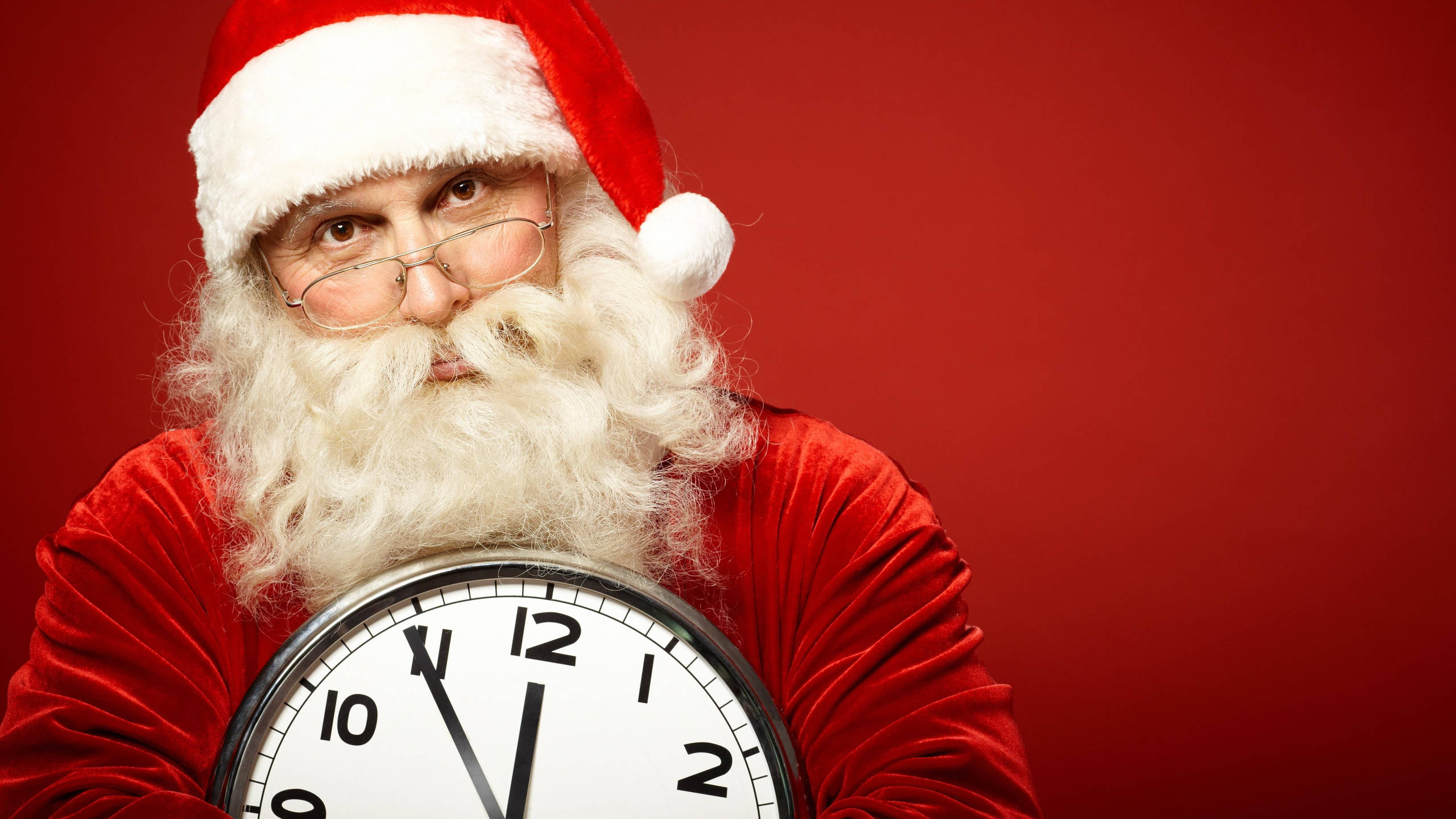 Santa Claus 桌布 壁紙 — 聖誕老人表情嚴肅，手持一個顯示接近午夜時鐘，背景為純紅色。