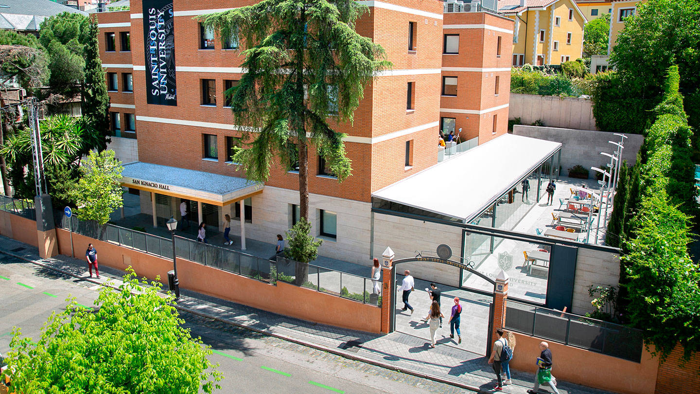 Architecture 桌布 壁紙 — 聖路易斯大學校園的鳥瞰圖，磚砌建築、茂密的綠樹和學生在陽光明媚的日子裡在拱門附近行走。
