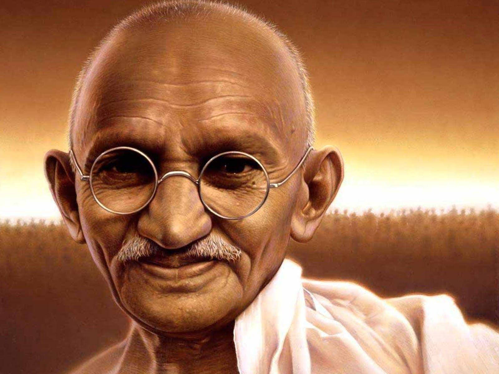 Mahatma Gandhi 桌布 壁紙 — 聖雄甘地的特寫肖像，戴著圓形眼鏡，肩上披著白色布料，背景是溫暖的金色。