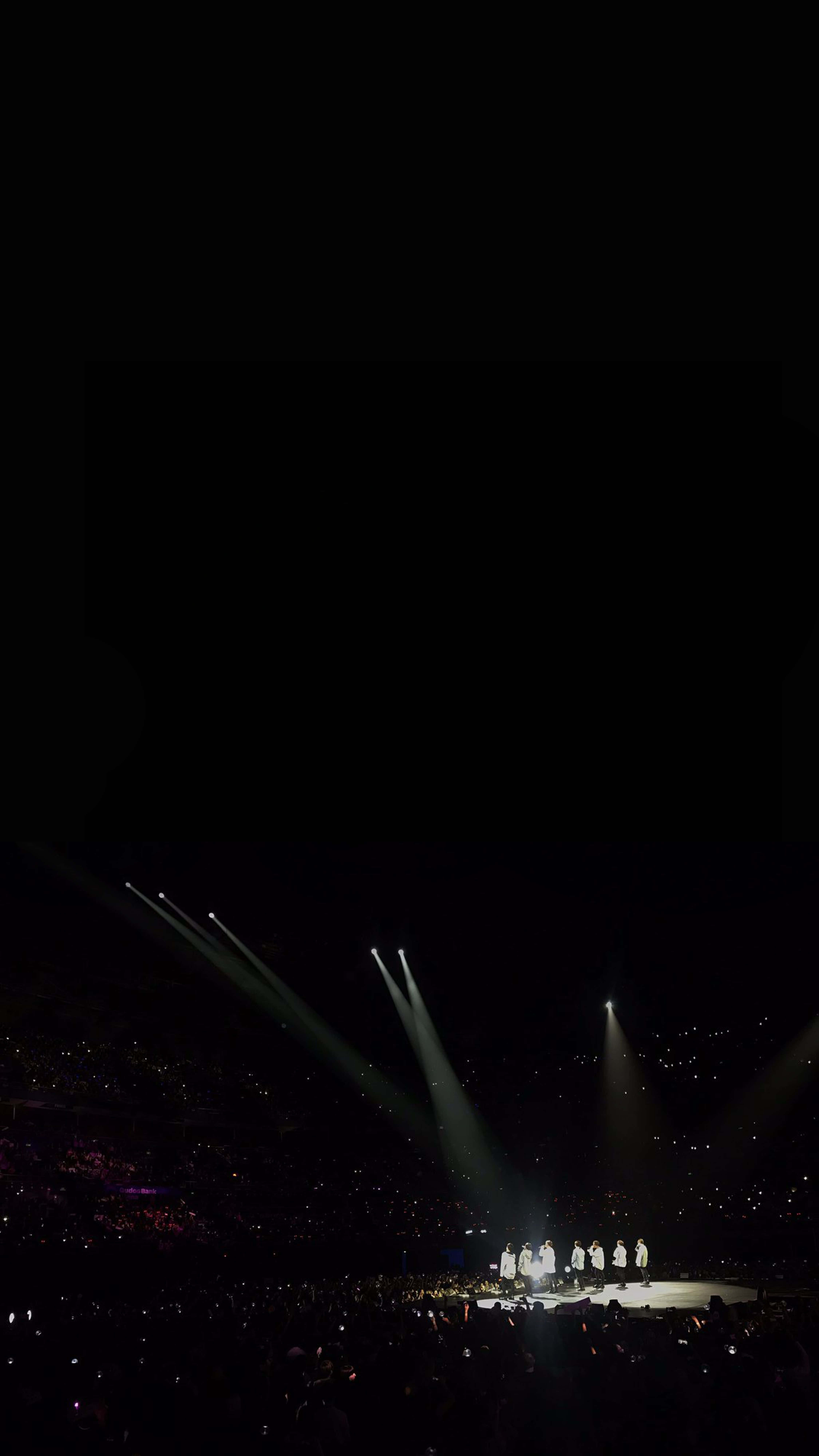 Bts Stage 桌布 壁紙 — 聚光燈光束照亮黑暗舞台上的表演者，前方是觀眾手機燈光的海洋。