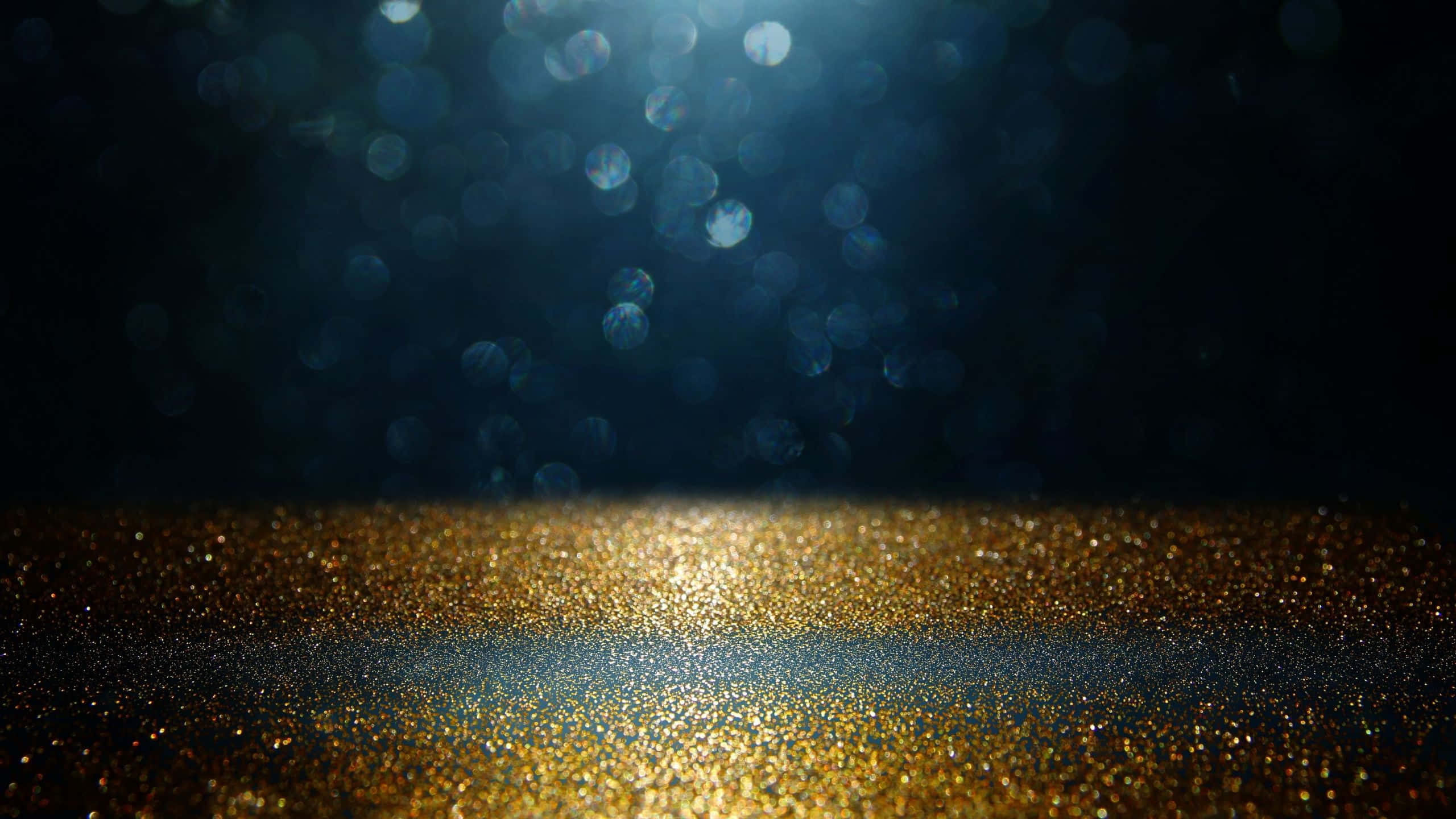 Black And Gold Glitter 桌布 壁紙 — 聚光燈照亮了黑暗背景下閃閃發光的金色表面，伴隨著柔和的藍色散景燈光。