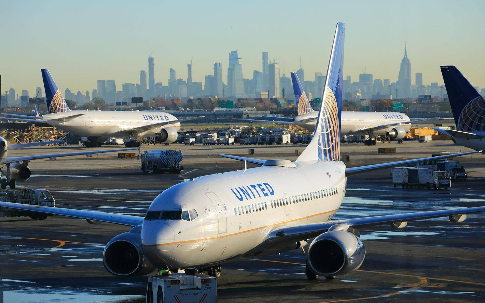 Airport 桌布 壁紙 — 聯合航空的噴射機停在濕滑的停機坪上，紐約市天際線在朦朧的晨光中可見。