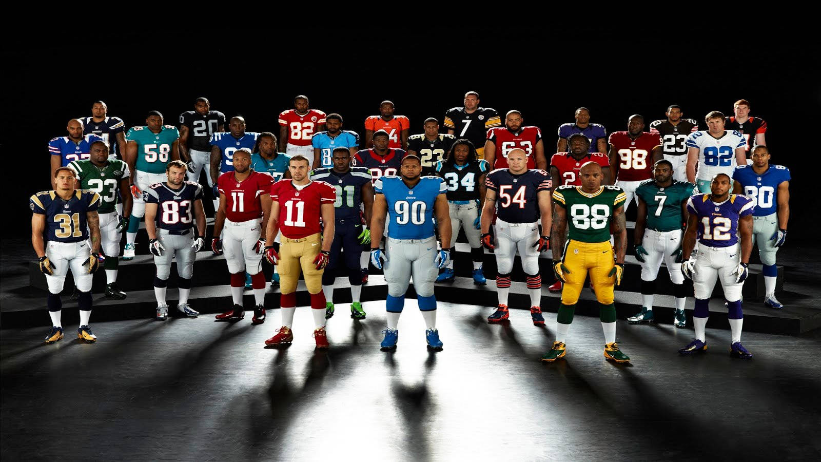 NFL 桌布 壁紙 — 職業美式足球運動員身穿隊服，在黑暗的舞台上於戲劇性的聚光燈下排成隊形。