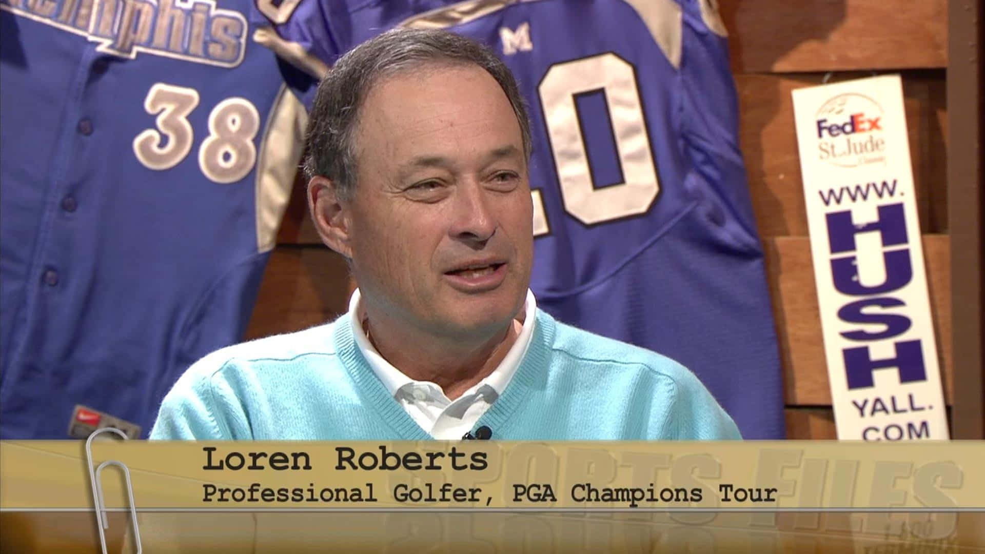 高爾夫 桌布 壁紙 — 職業高爾夫球手 Loren Roberts 在一個背後有藍色運動球衣和 FedEx St Jude 標誌的錄影室中發言。