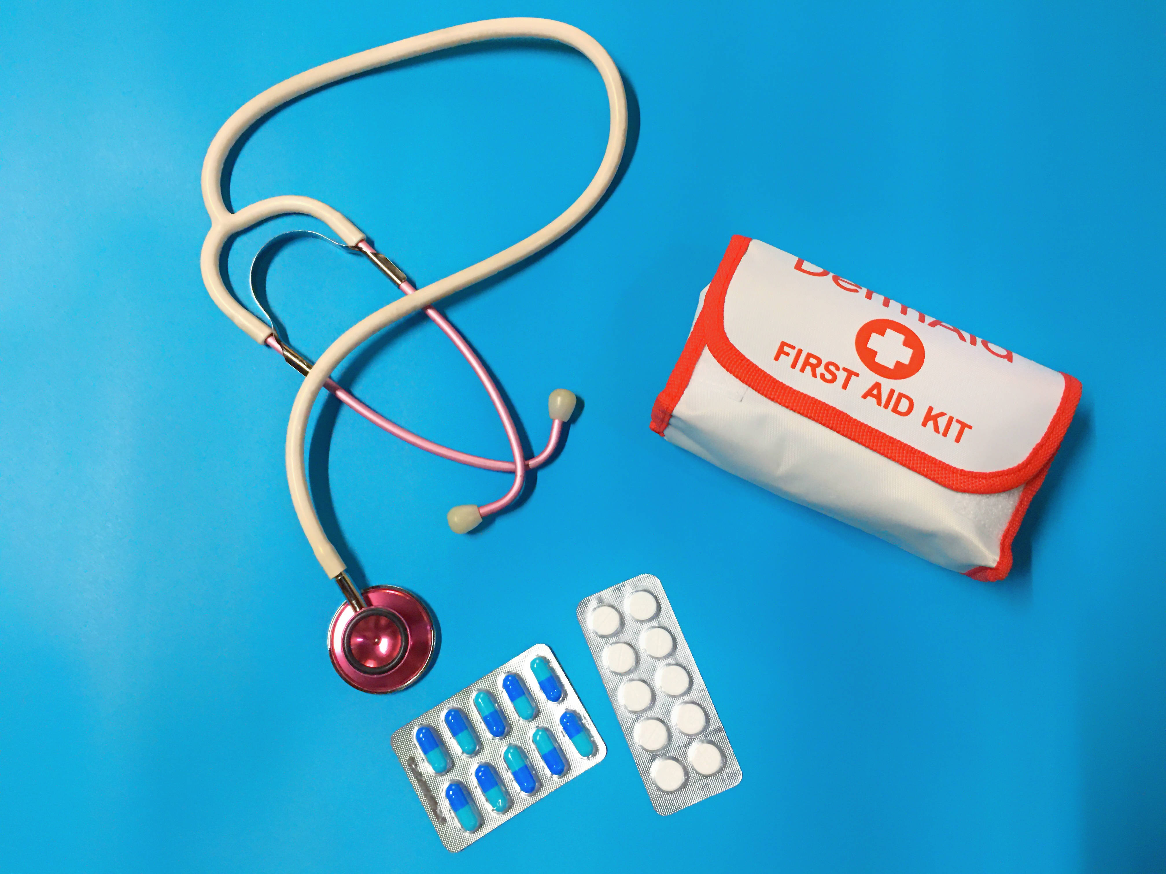 Stethoscope 桌布 壁紙 — 聽診器、藥丸和急救箱整齊地排列在鮮豔的藍色背景上。