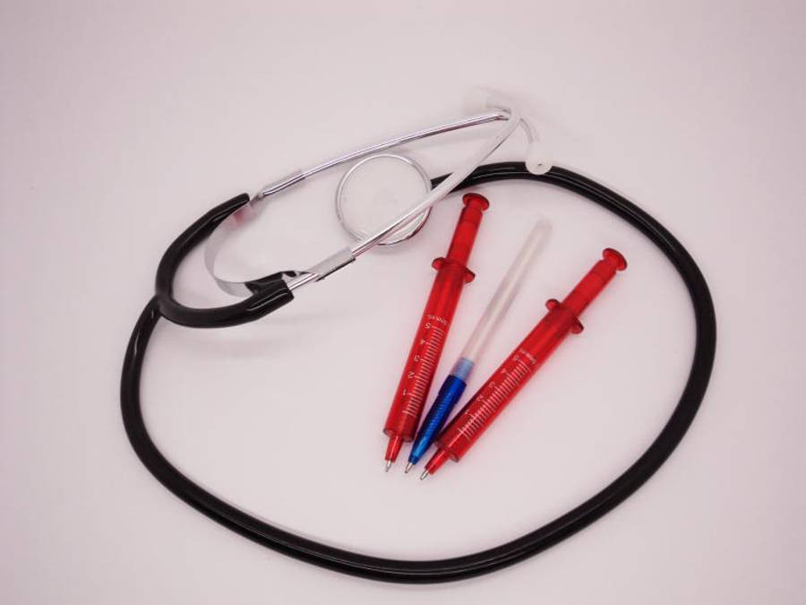 Stethoscope 桌布 壁紙 — 聽診器和注射器形狀的筆整齊地排列在純白色背景上，帶有乾淨的攝影棚燈光。