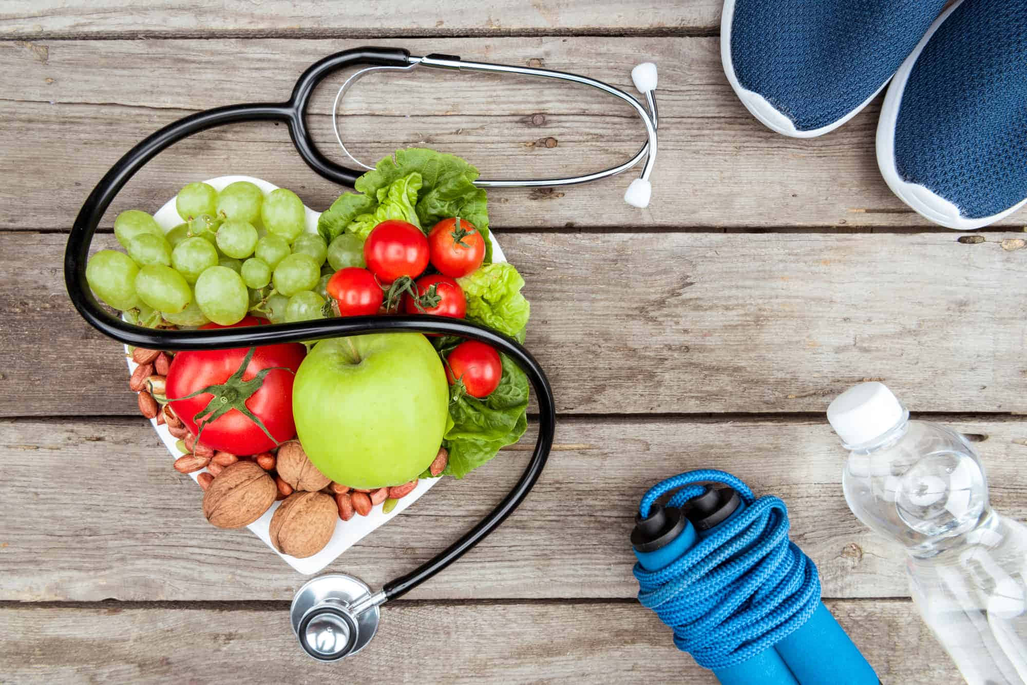 Health 桌布 壁紙 — 聽診器在木質表面上圍繞一盤新鮮水果、蔬菜、堅果和生菜形成心形，附近有運動鞋、跳繩和水瓶。