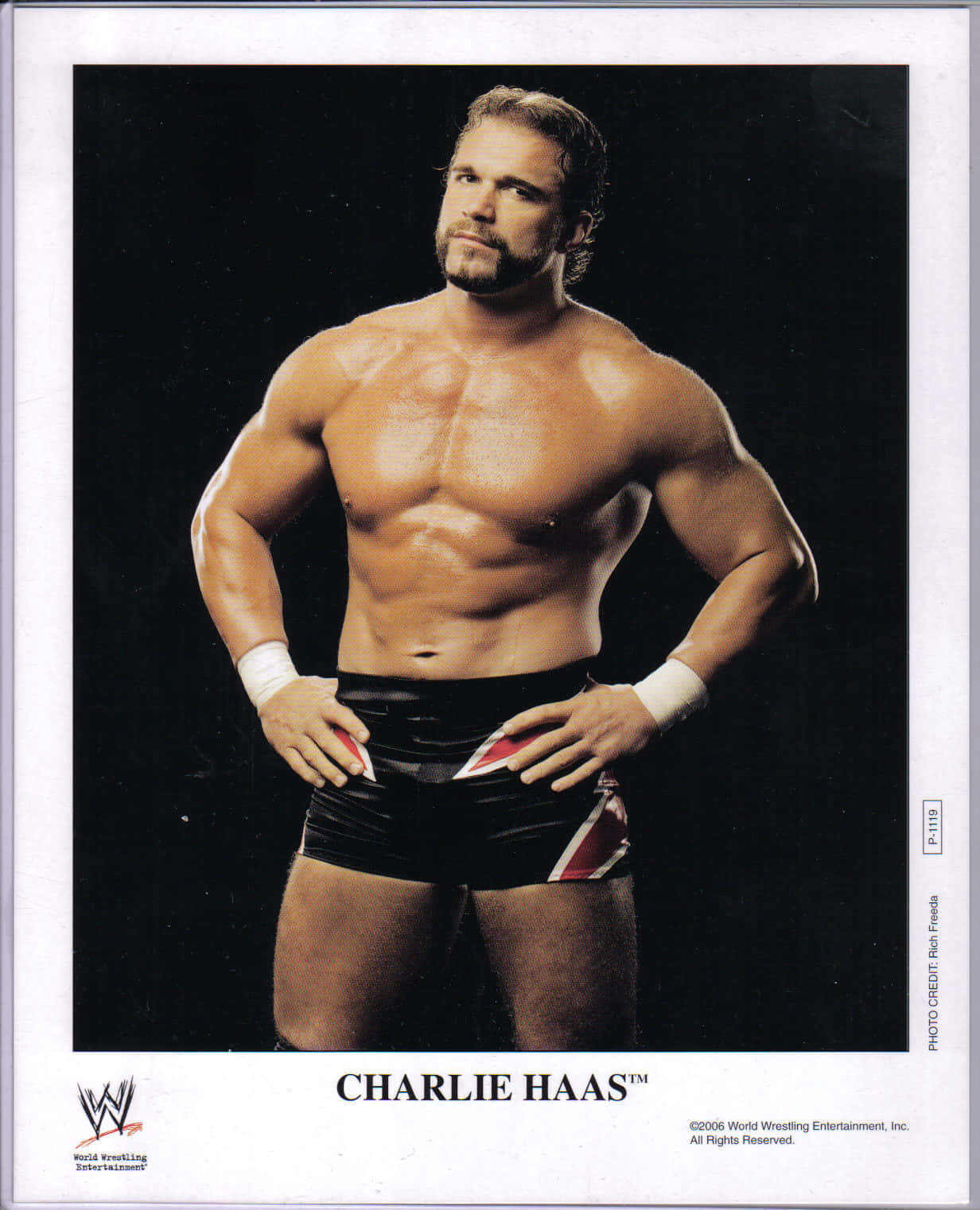 Charlie Haas 桌布 壁紙 — 肌肉發達的摔角手 Charlie Haas 穿著黑色摔角短褲，在深色工作室背景前自信地擺姿勢。