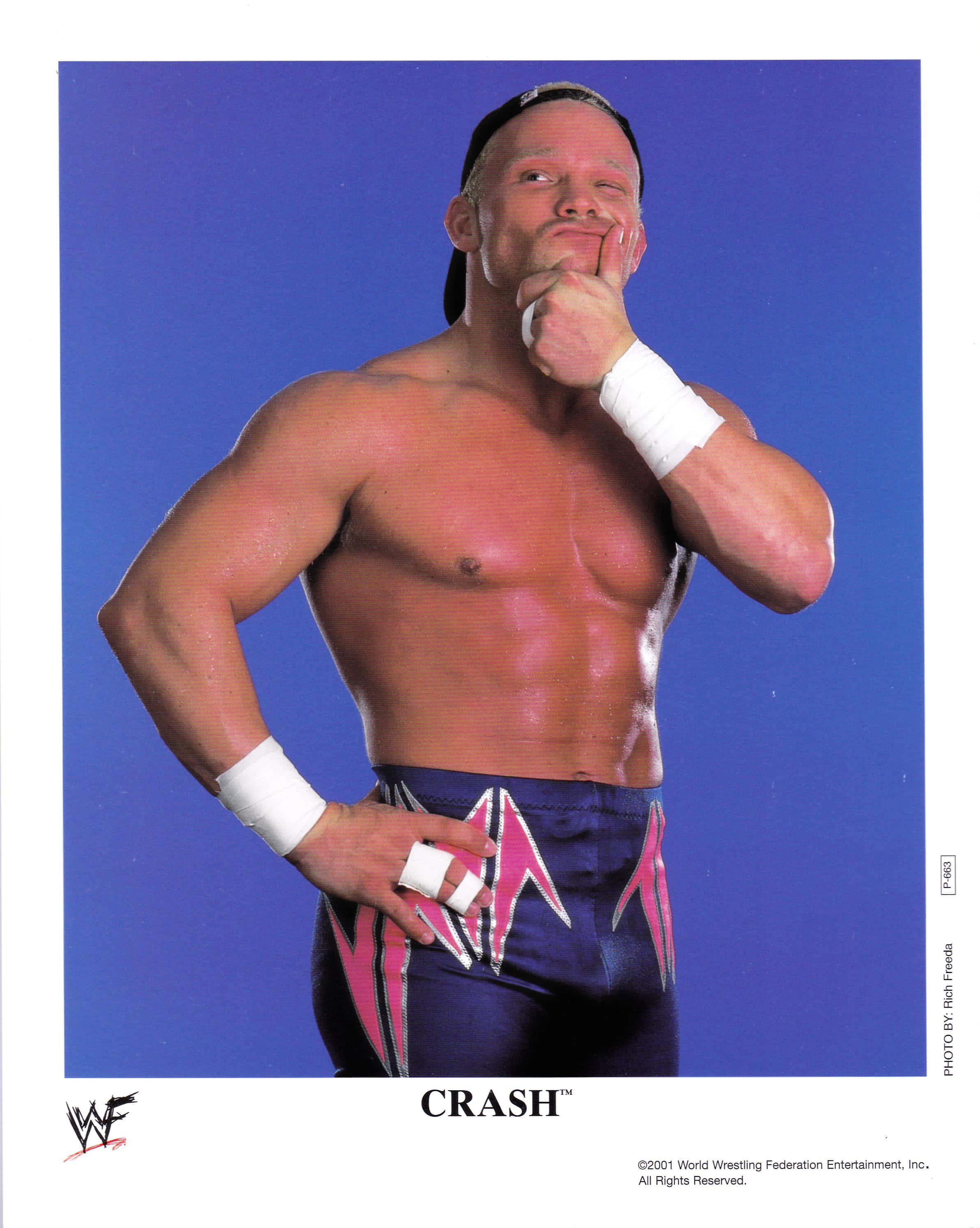 Crash Holly 桌布 壁紙 — 肌肉發達的摔角手 Crash 穿著藍色短褲，帶有粉紅色閃電，在純藍色工作室背景前自信地擺姿勢。