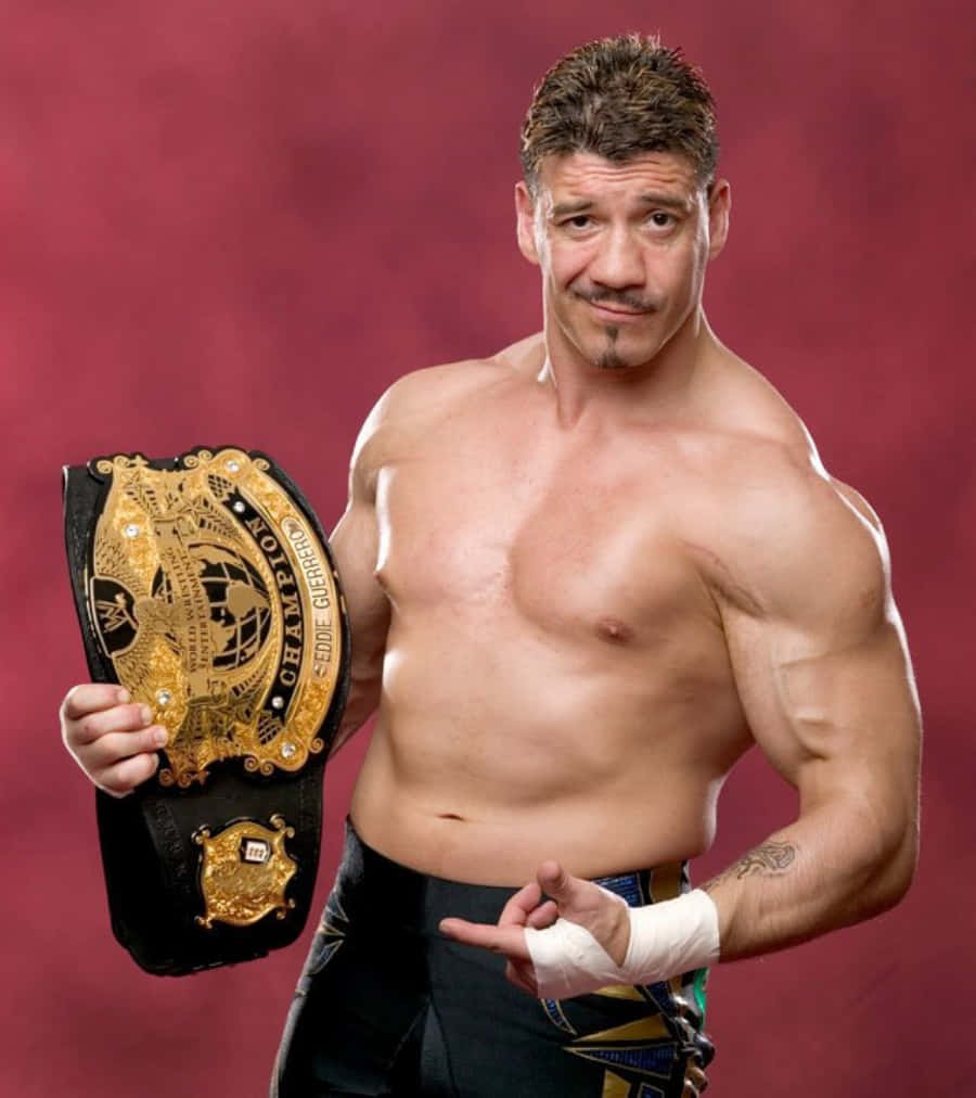 WWE 桌布 壁紙 — 肌肉發達的摔角手 Eddie Guerrero 自信地擺姿勢，手持 WWE Intercontinental Championship 腰帶，背景是深紅色的攝影棚。