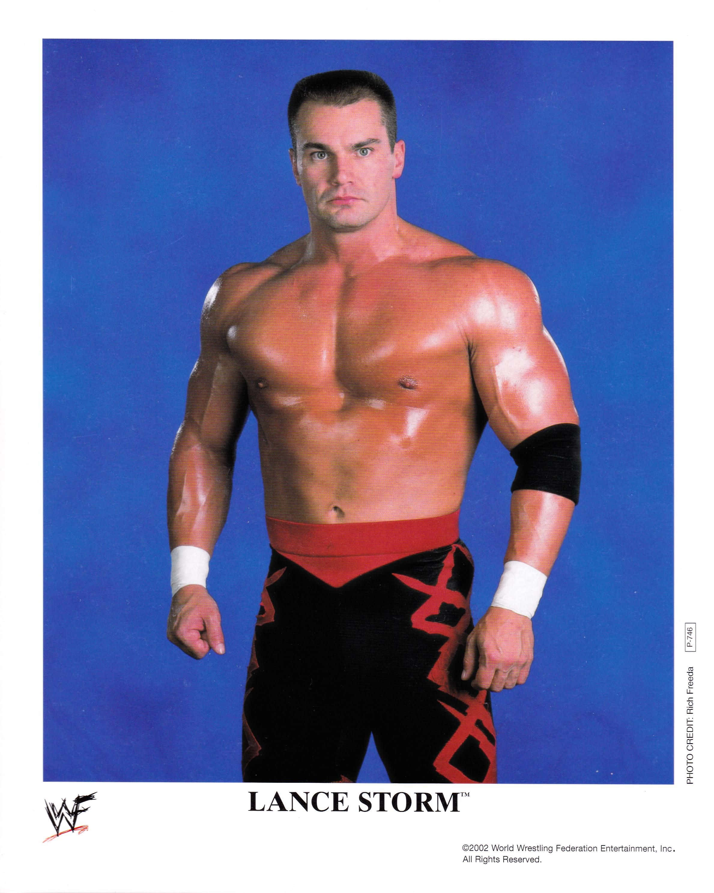 Canadian 桌布 壁紙 — 肌肉發達的摔角手 Lance Storm 赤裸上身，在純藍色攝影棚背景前擺姿勢，穿著紅黑相間的短褲。
