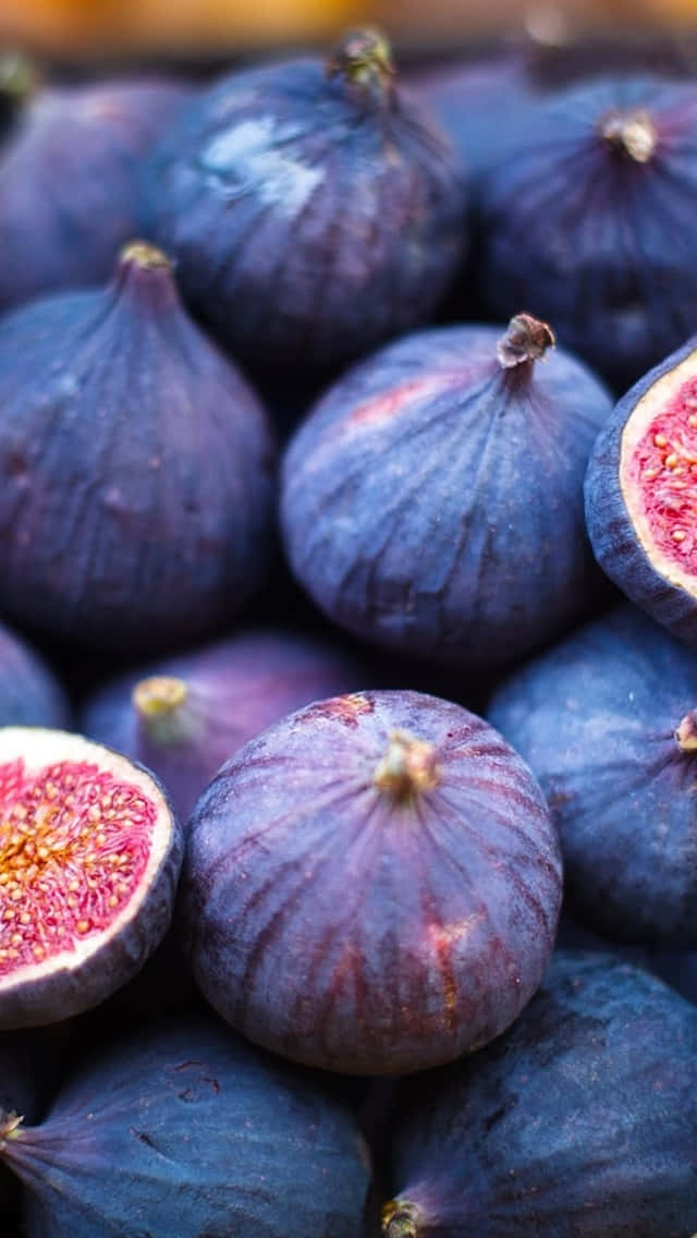 Purple Figs 桌布 壁紙 — 肥美紫色無花果的特寫，其中一個切開一半，露出多汁的粉紅色果肉和金色種子。