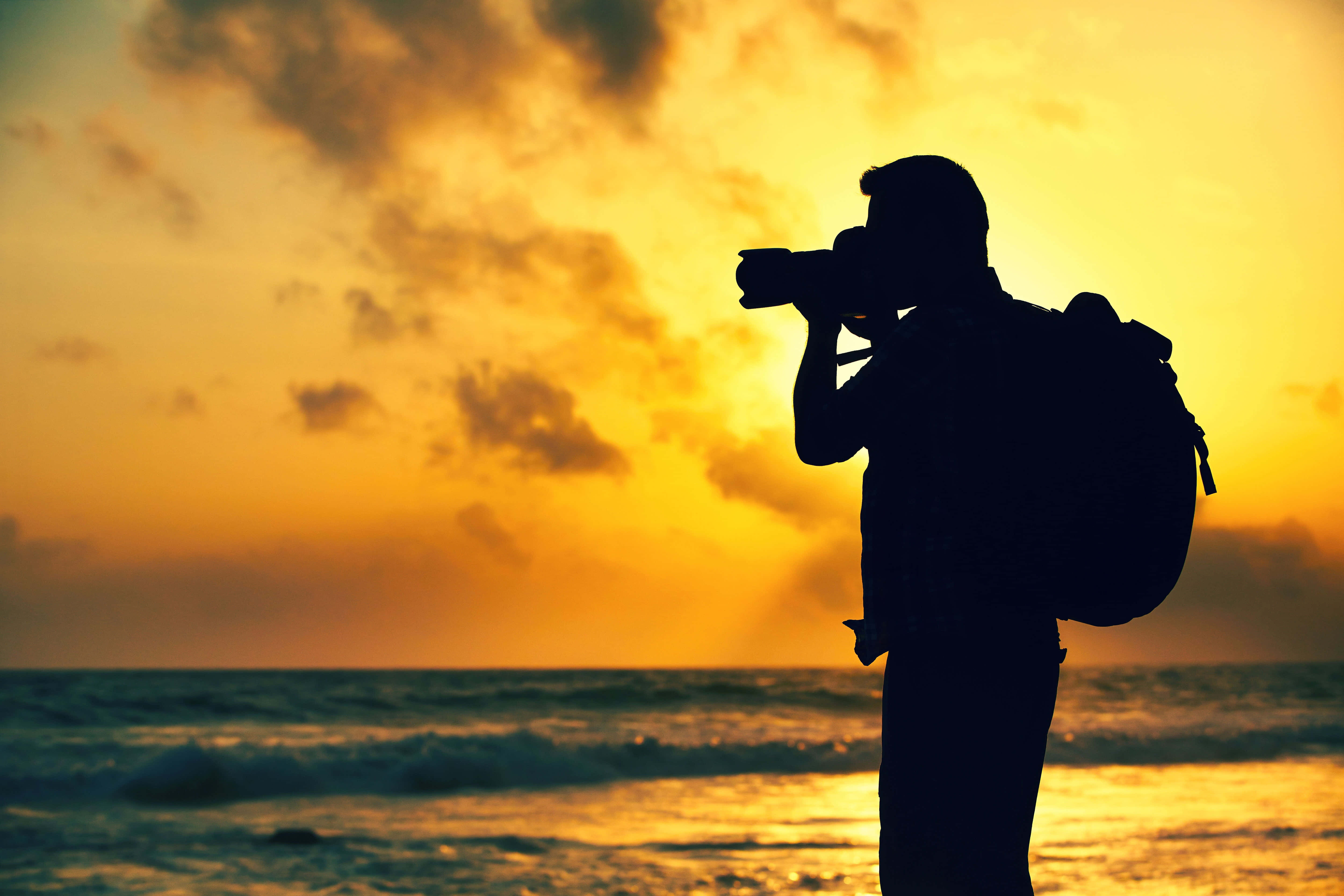 Dslr 桌布 壁紙 — 背著背包的攝影師剪影，捕捉海洋波浪上的日落。